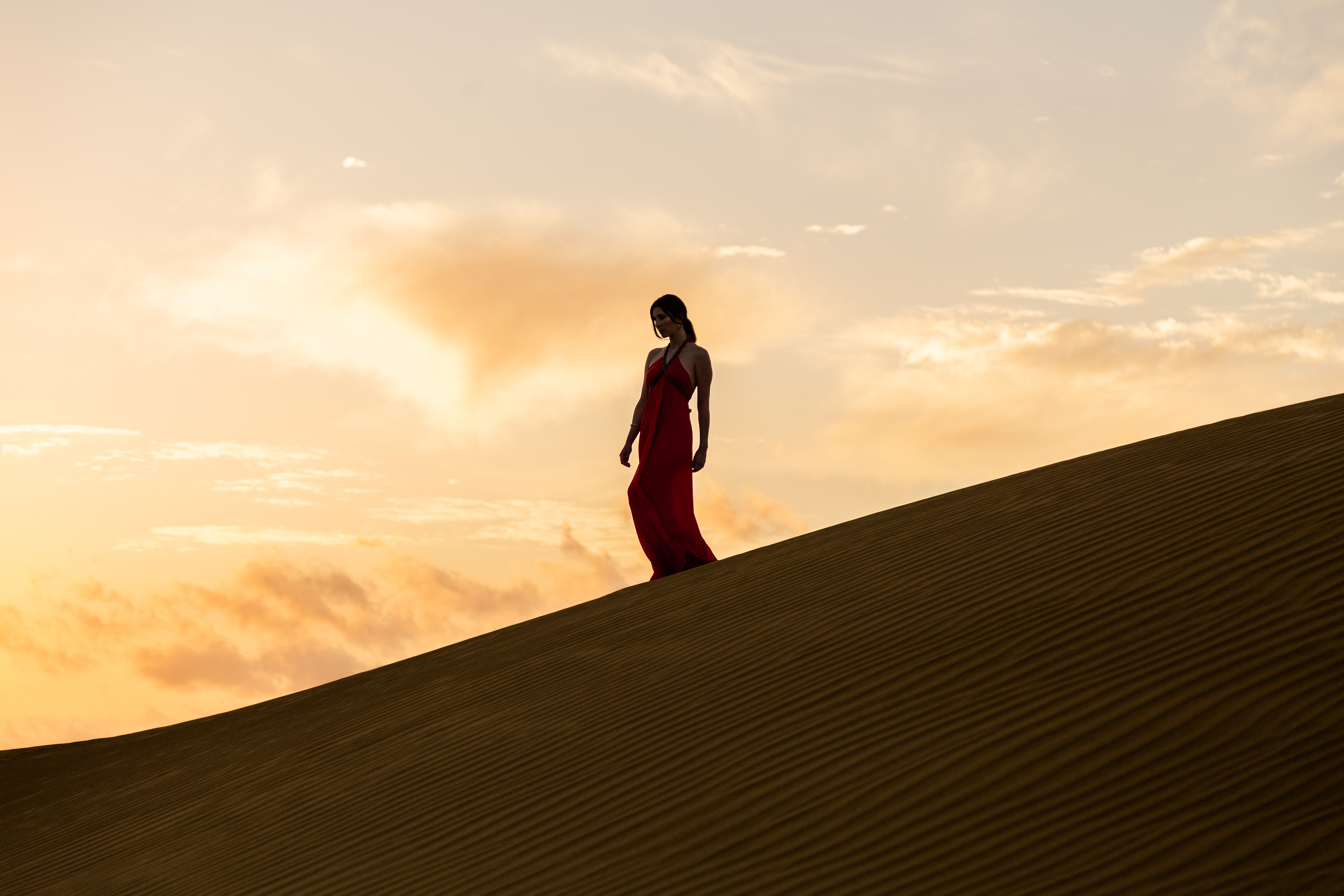 a woman in a red dress walking up a sand dune