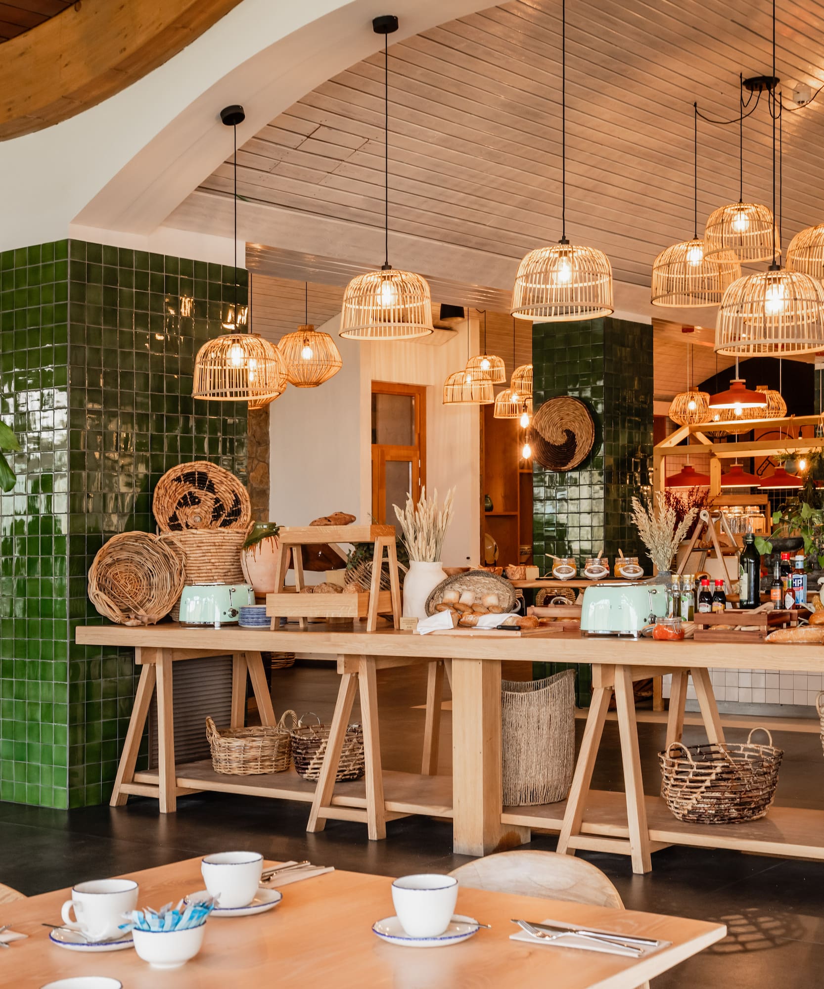 Hotel restaurant breakfast buffet with green tiles, rattan lights, and natural decor.