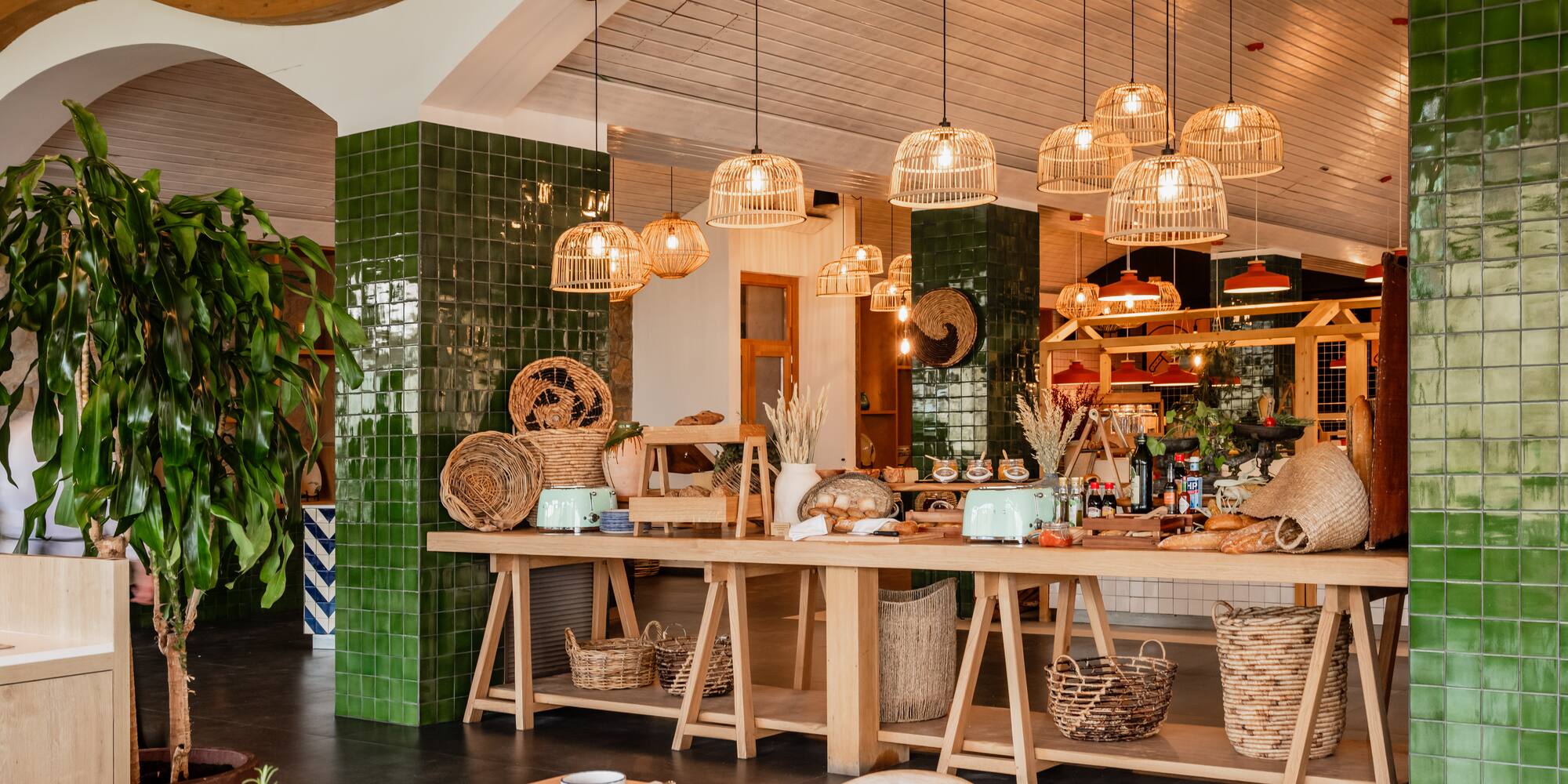 Stylish restaurant interior with buffet, wicker lights, green tiles, and wooden tables.