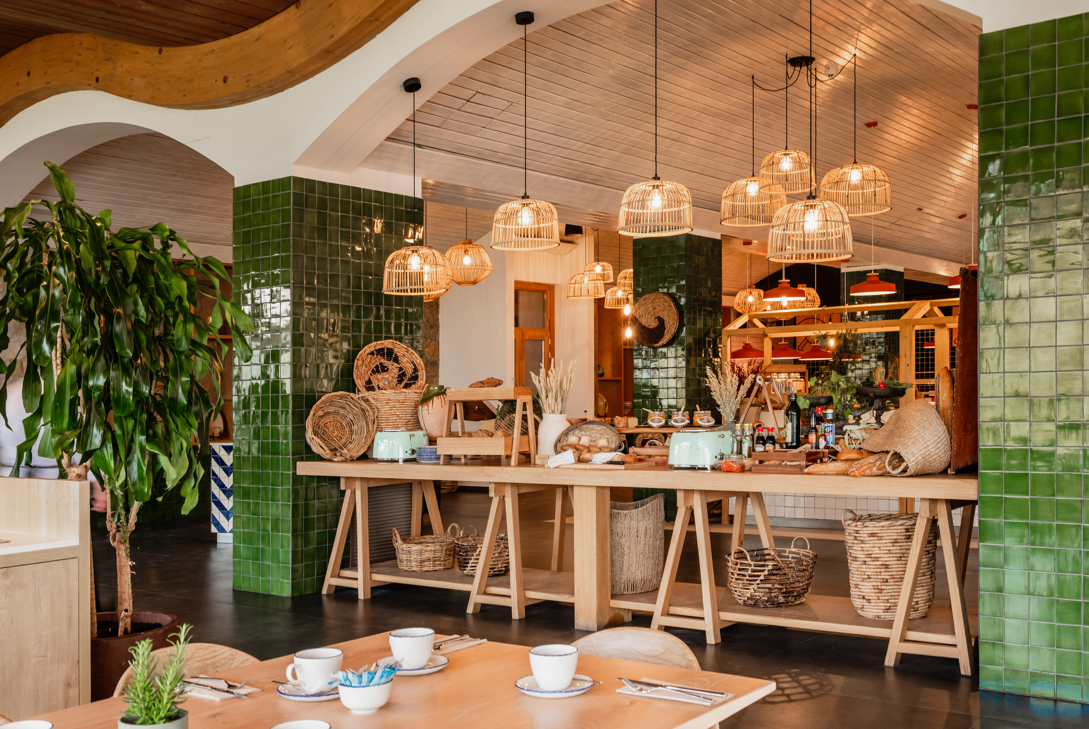 Stylish restaurant interior with buffet, wicker lights, green tiles, and wooden tables.
