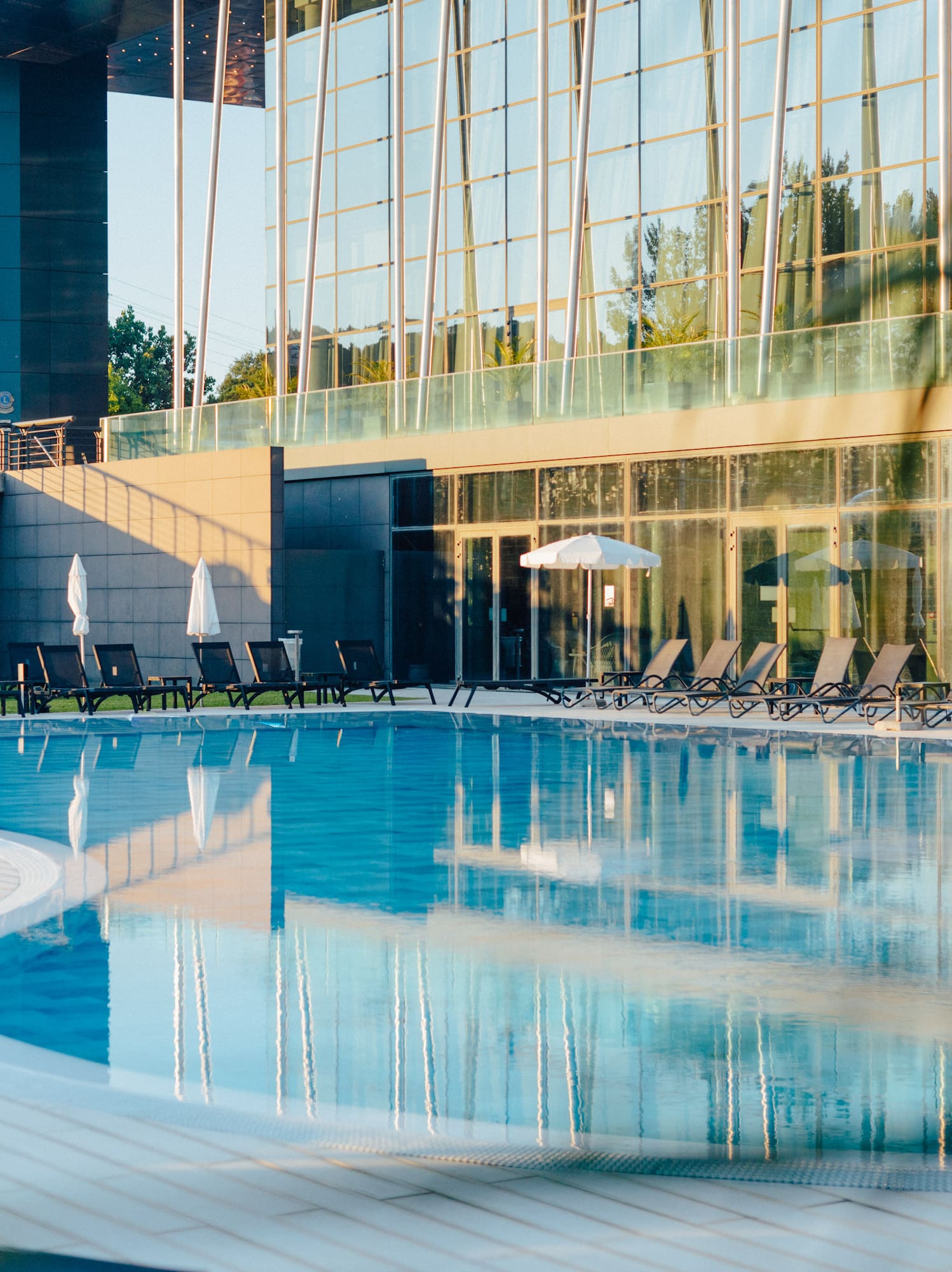 Luxury outdoor swimming pool with lounge chairs and glass building facade background. - Meliá Braga, Braga