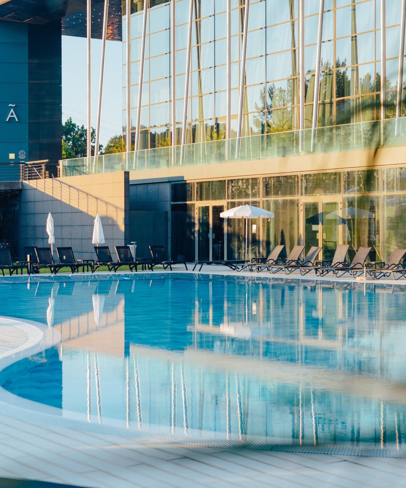 Luxury hotel swimming pool with lounge chairs and modern glass architecture. - Meliá Braga, Braga