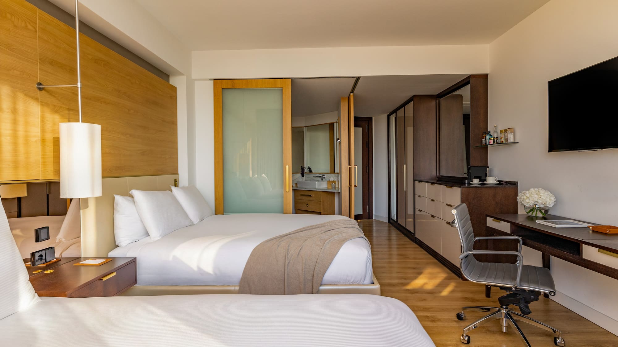 Modern hotel room with two beds, workstation, and open-plan bathroom.