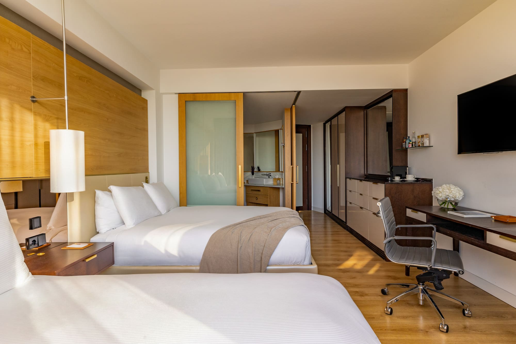 Modern hotel room with two beds, workstation, and open-plan bathroom.
