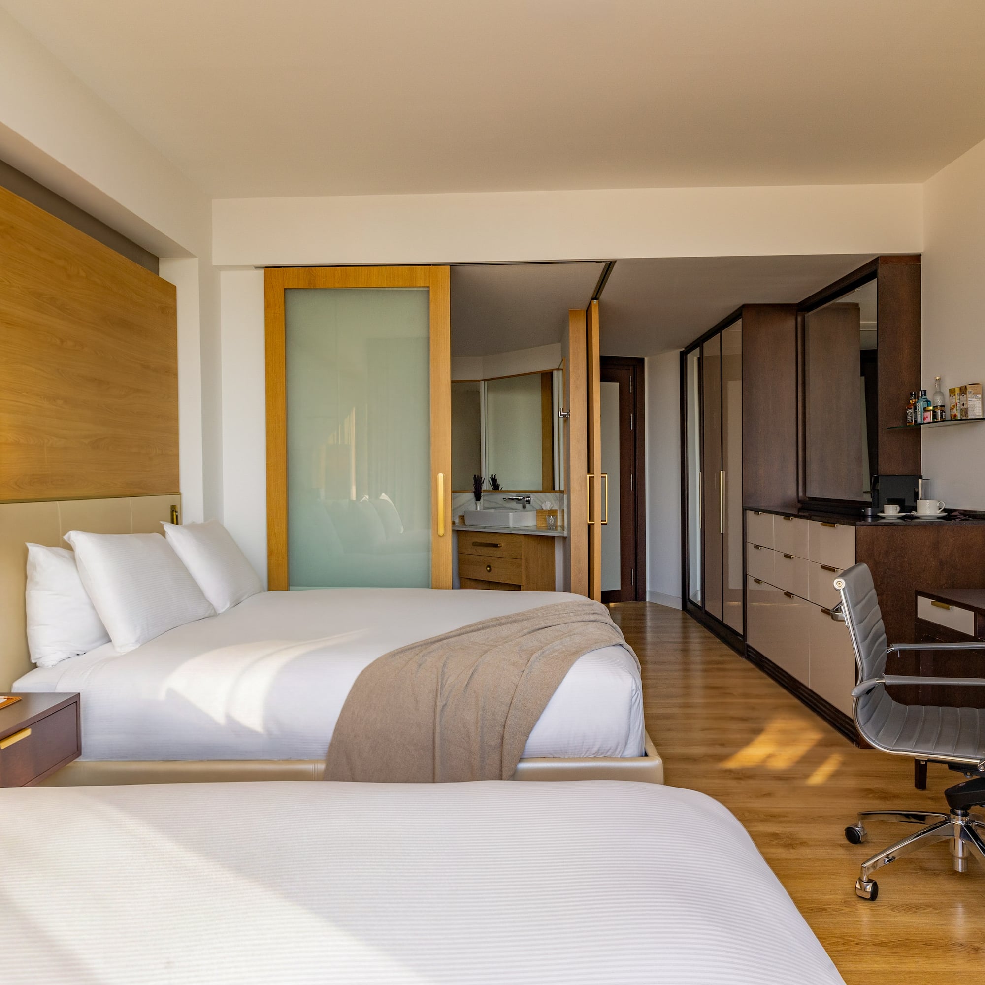 Modern hotel room with two beds, workstation, and open-plan bathroom.
