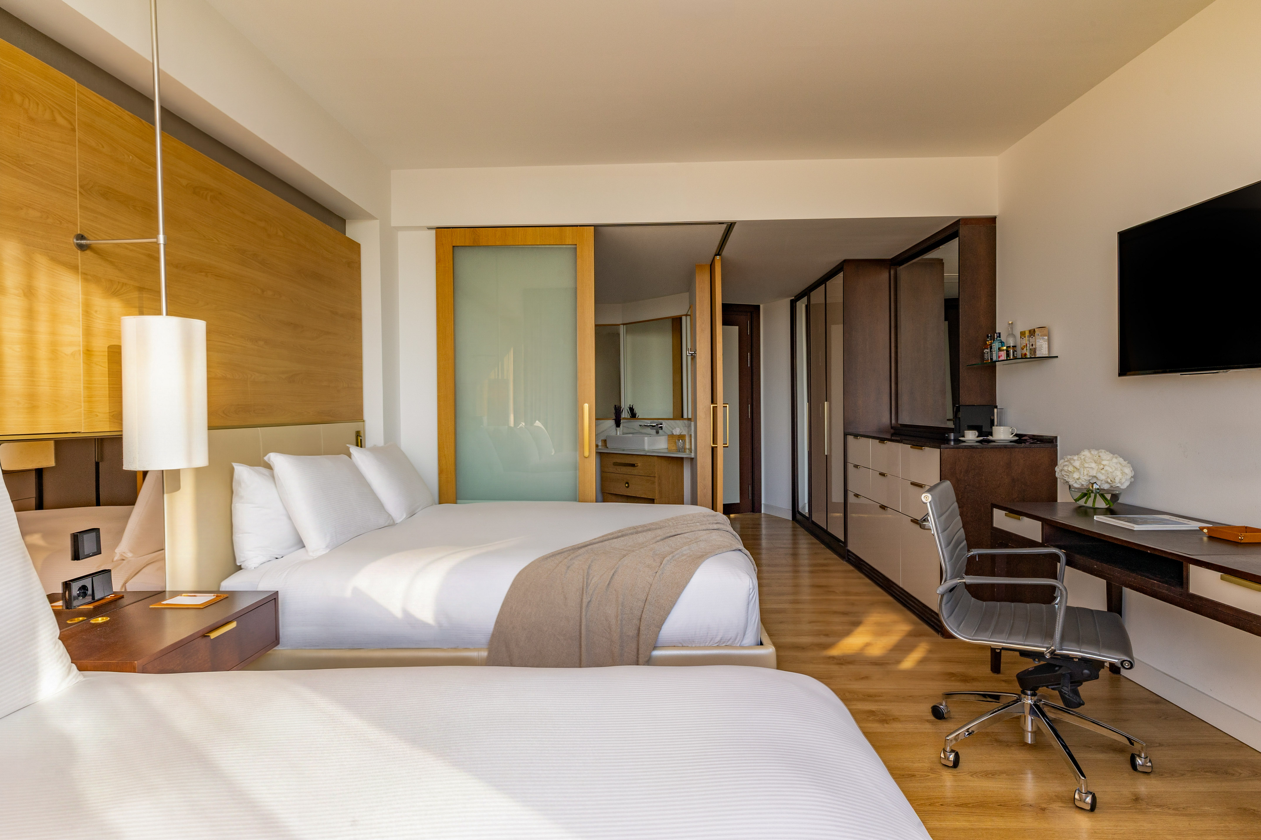 Modern hotel room with two beds, workstation, and open-plan bathroom.