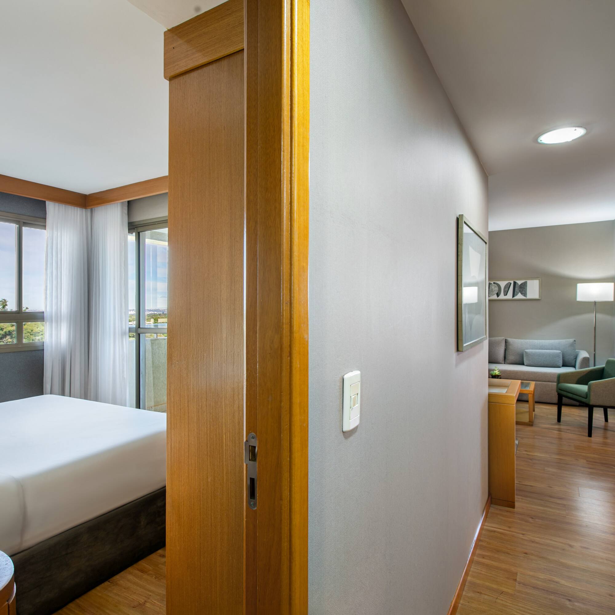 Bright hotel suite featuring bedroom, living room, large windows, and balcony.