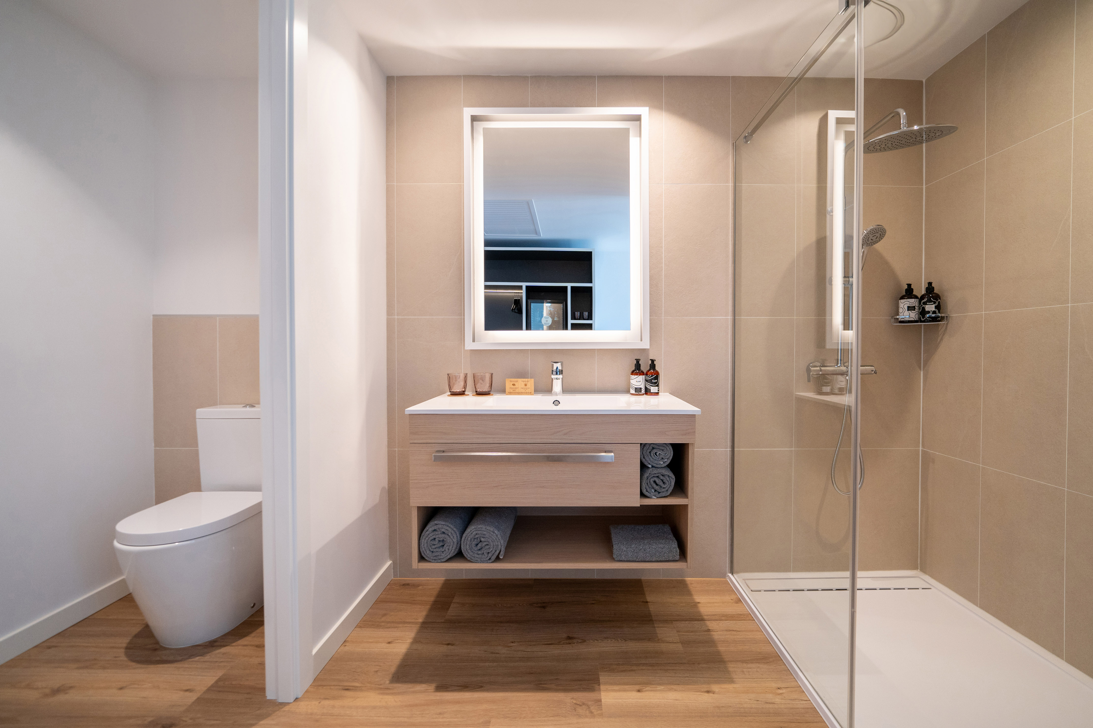 Contemporary bathroom with wood vanity, illuminated mirror, and tiled shower.