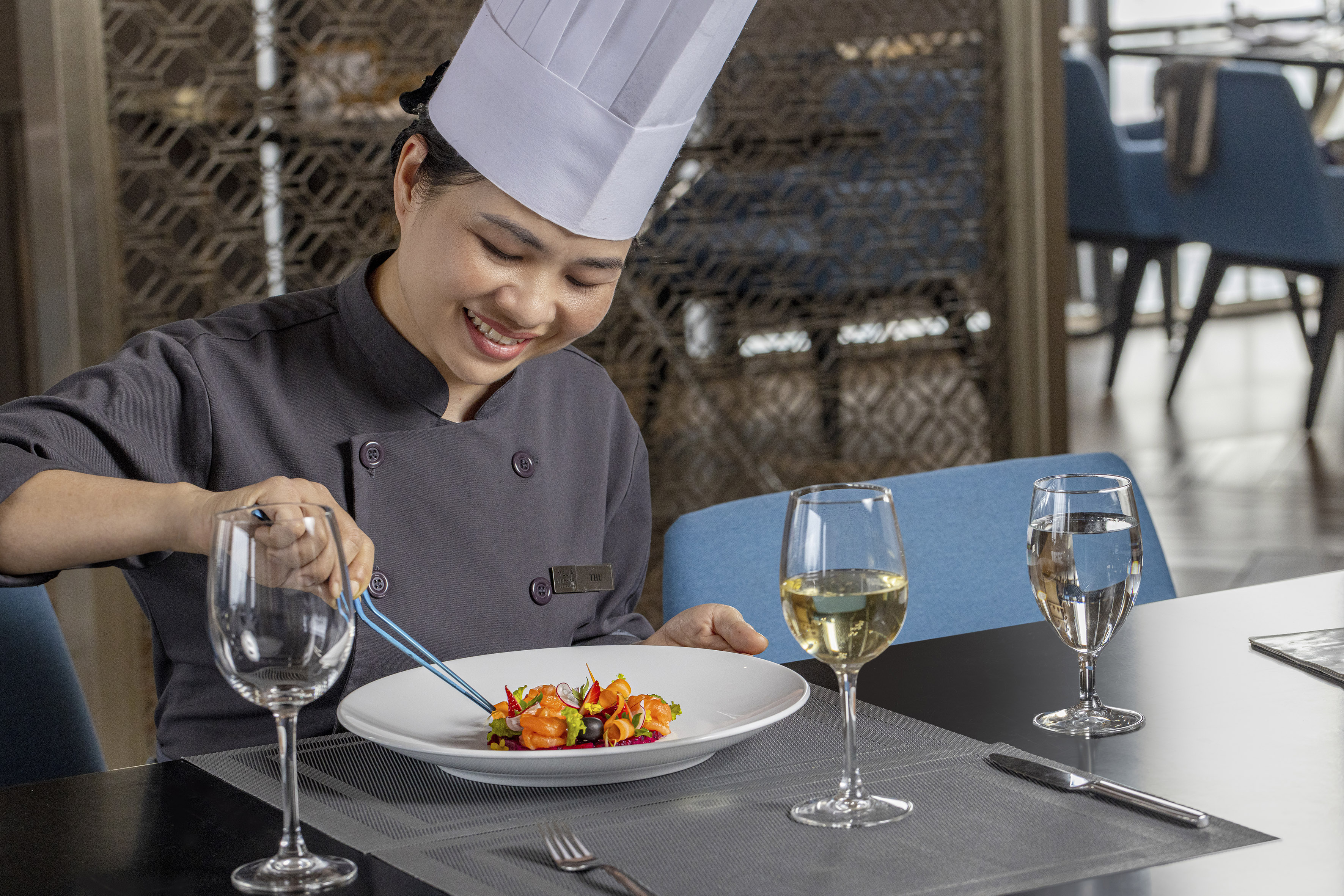 Smiling chef expertly plating a gourmet salmon appetizer in a restaurant.