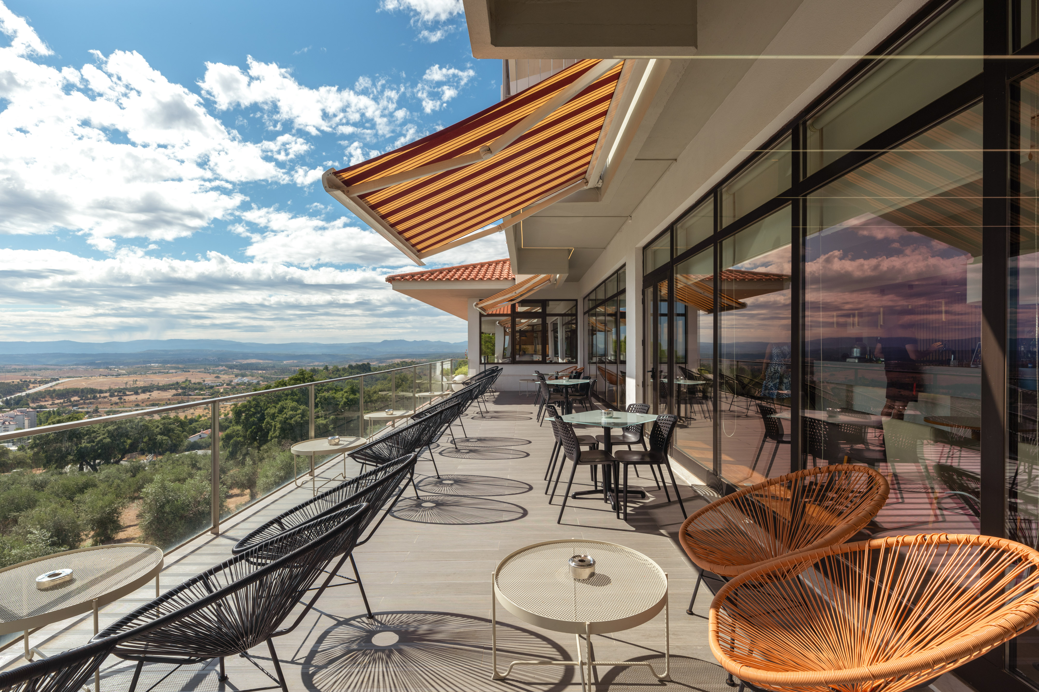 Outdoor terrace with panoramic mountain views, striped awnings, and stylish seating.