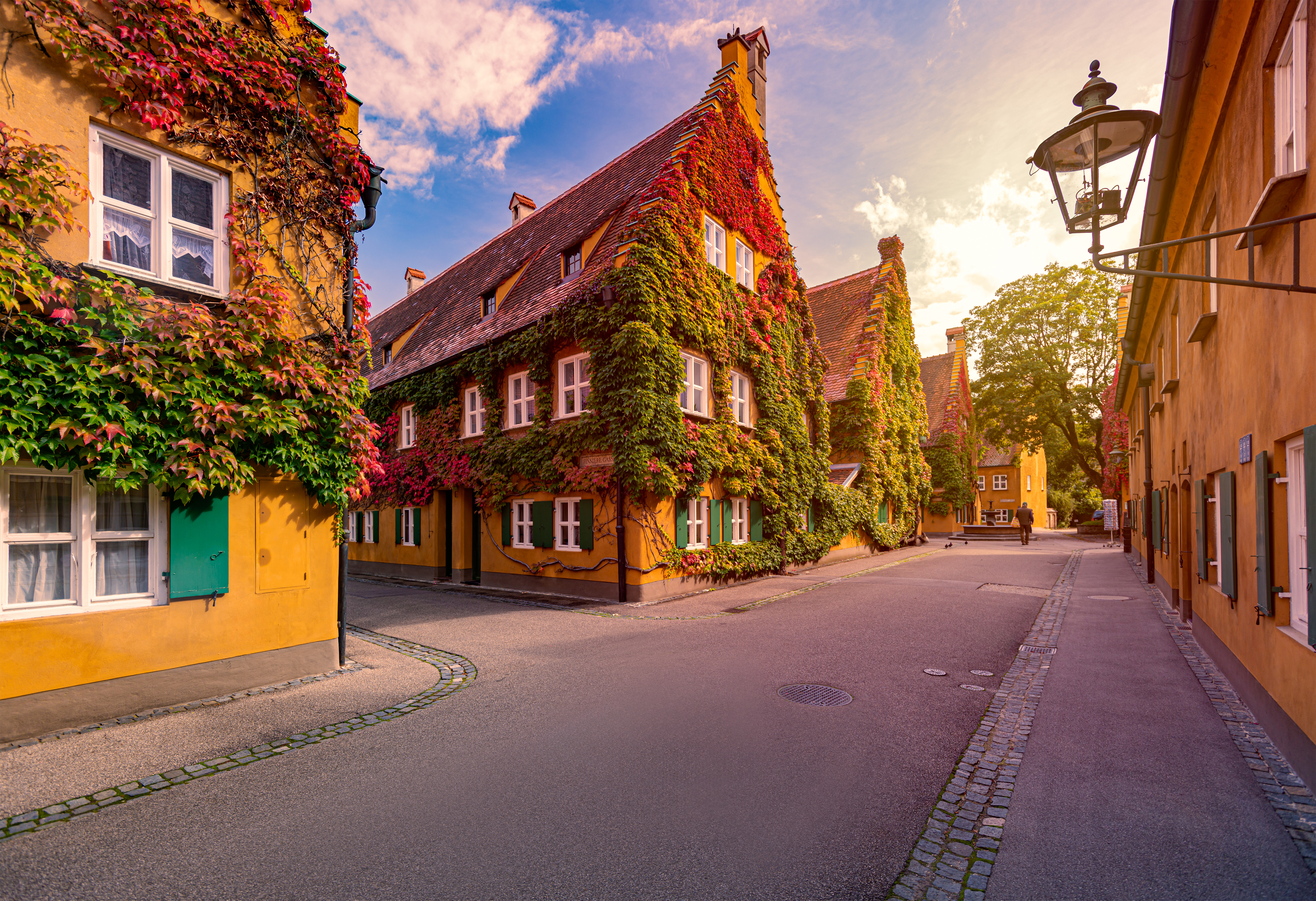 Colorful ivy-covered historic buildings on a cobblestone street at golden hour.