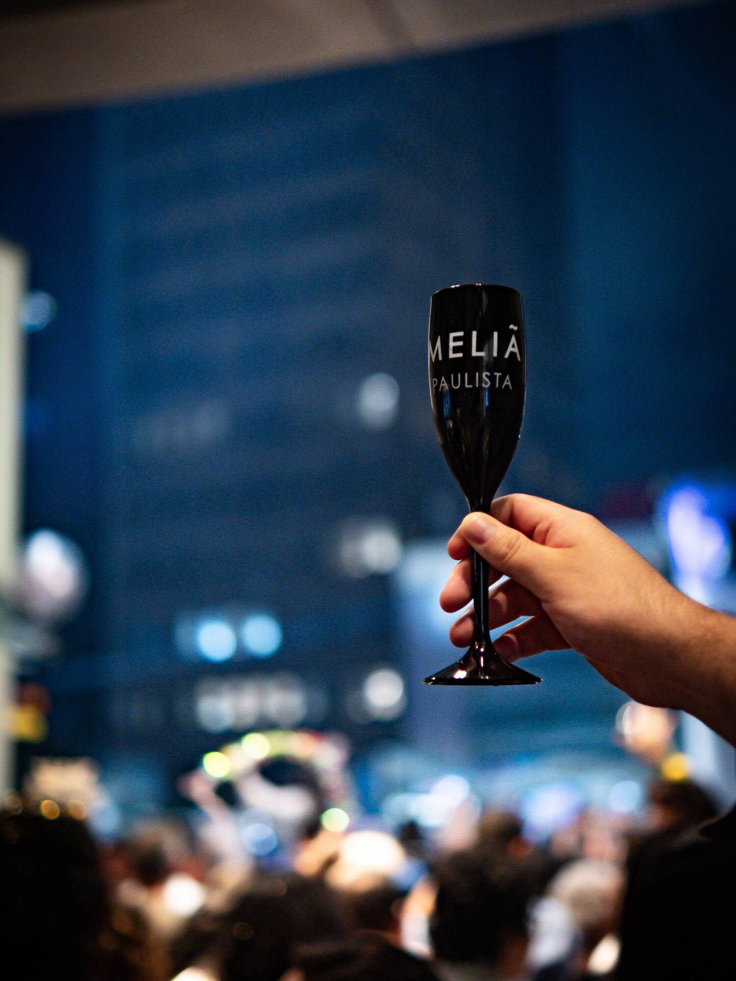 Hand holding Meliá Paulista champagne flute at a lively hotel event.