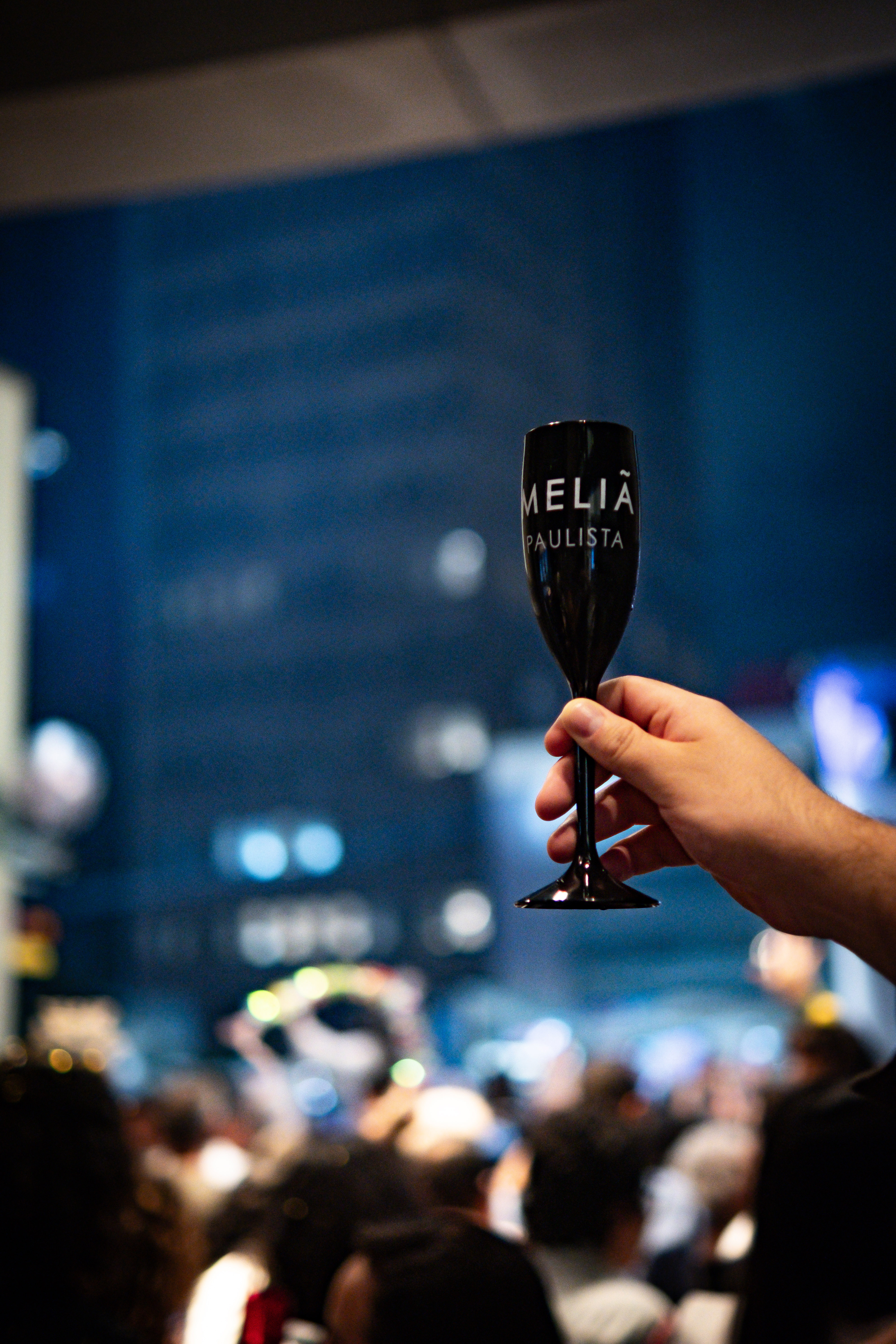 Hand holding Meliá Paulista champagne flute at a lively hotel event.
