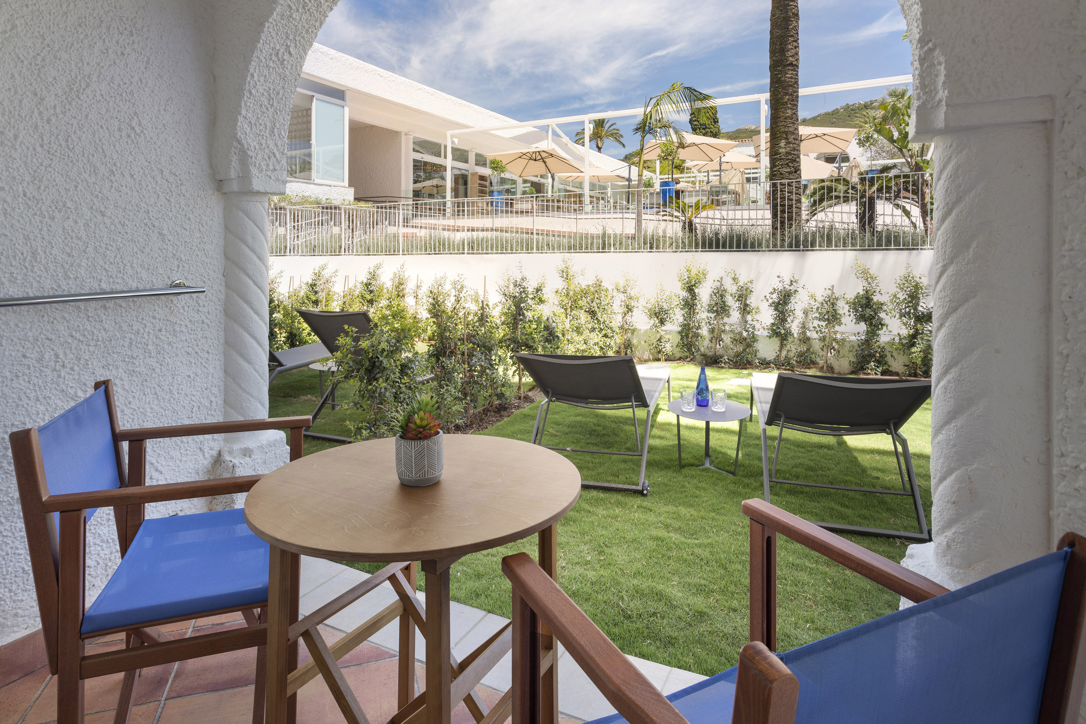 Hotel patio with blue chairs, grassy yard, sun loungers, and resort building.