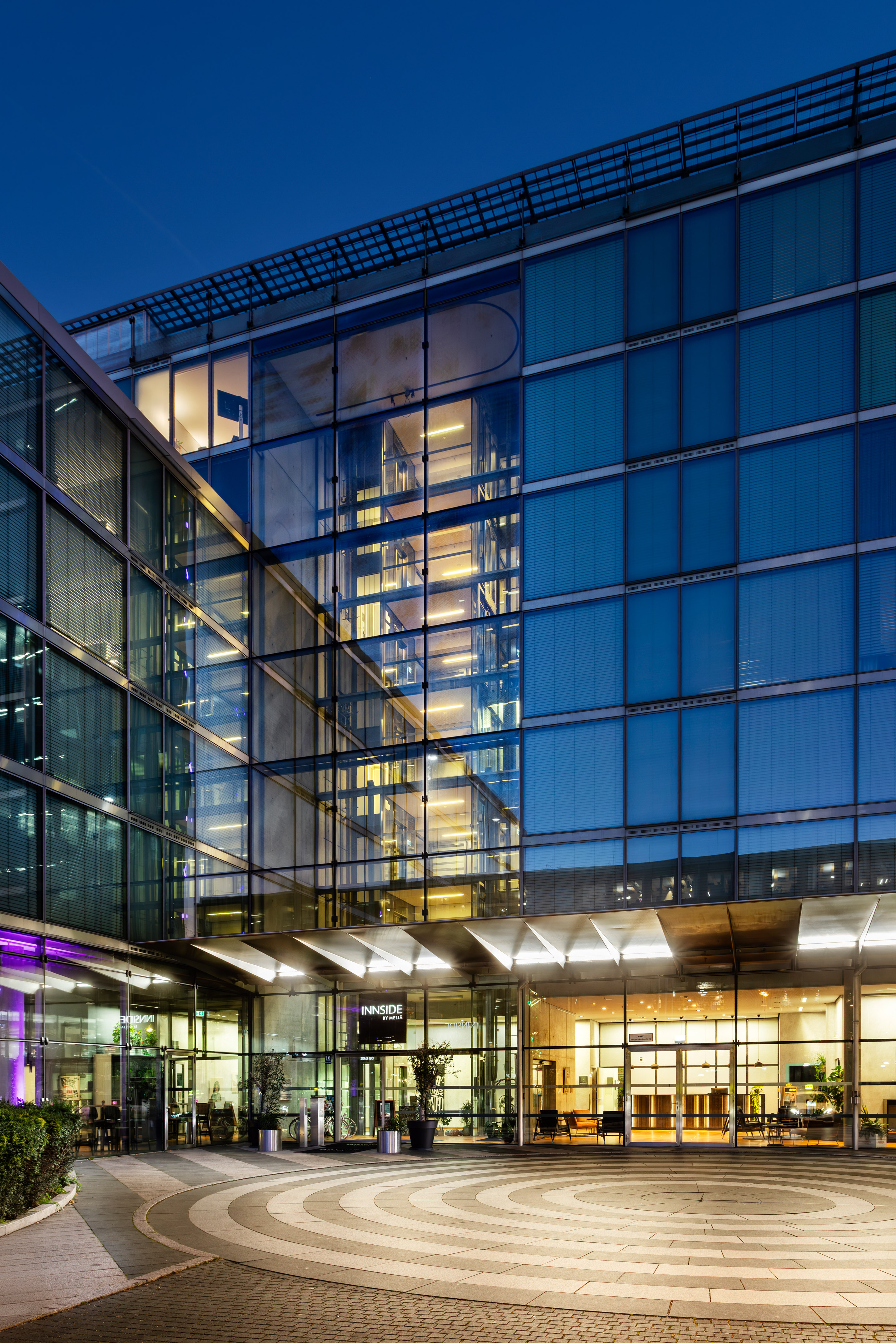 Modern glass hotel building entrance at night, showing "INNSiDE by MELIA" sign.