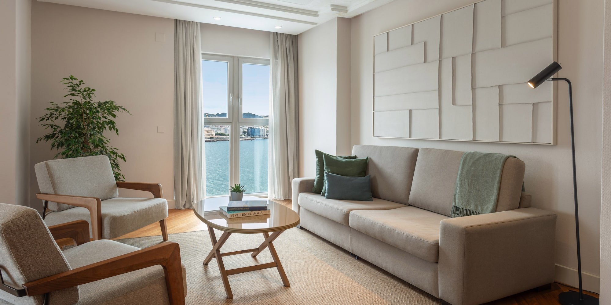 Salón moderno de apartamento con sofá, sillones y vistas al mar.