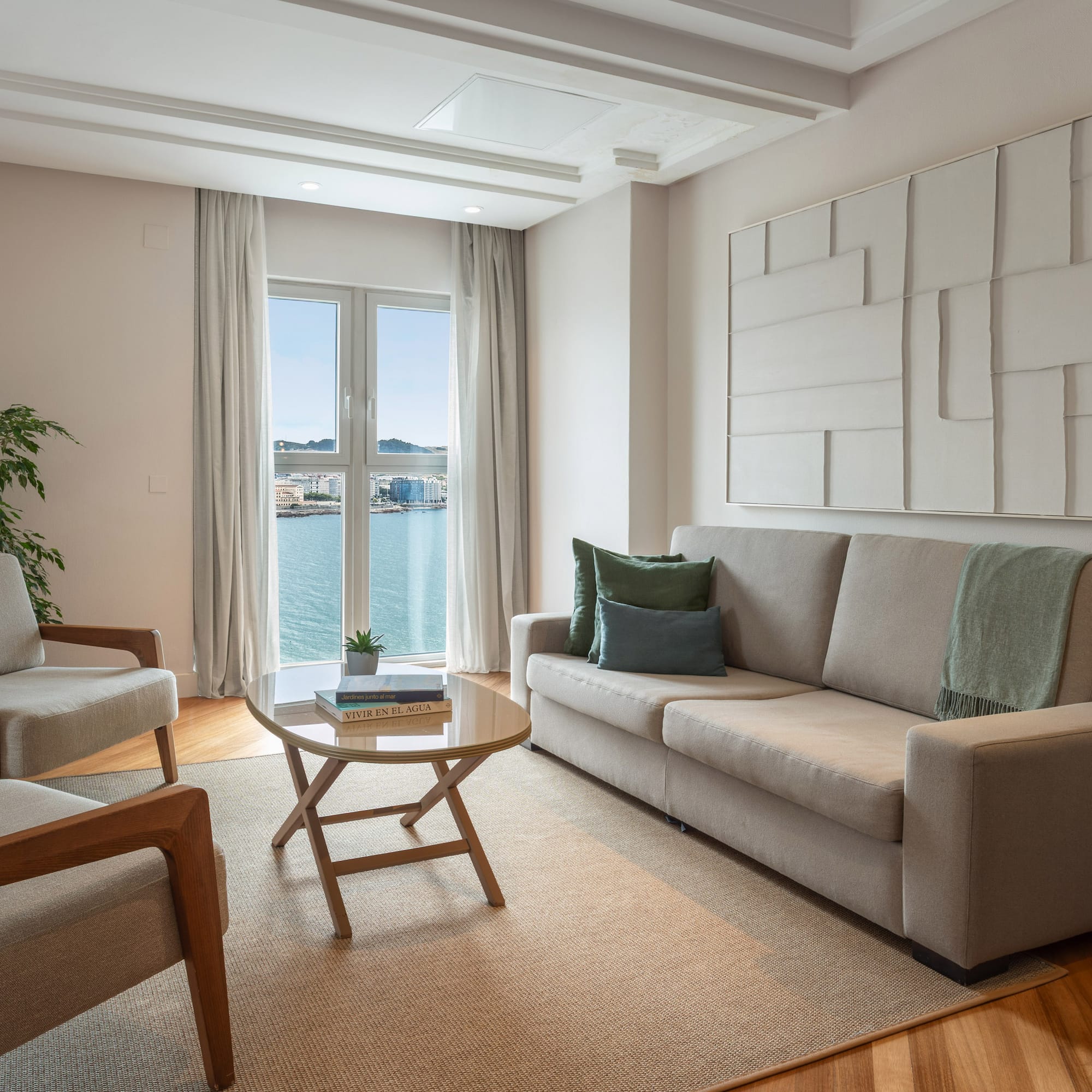 Salón moderno de apartamento con sofá, sillones y vistas al mar.
