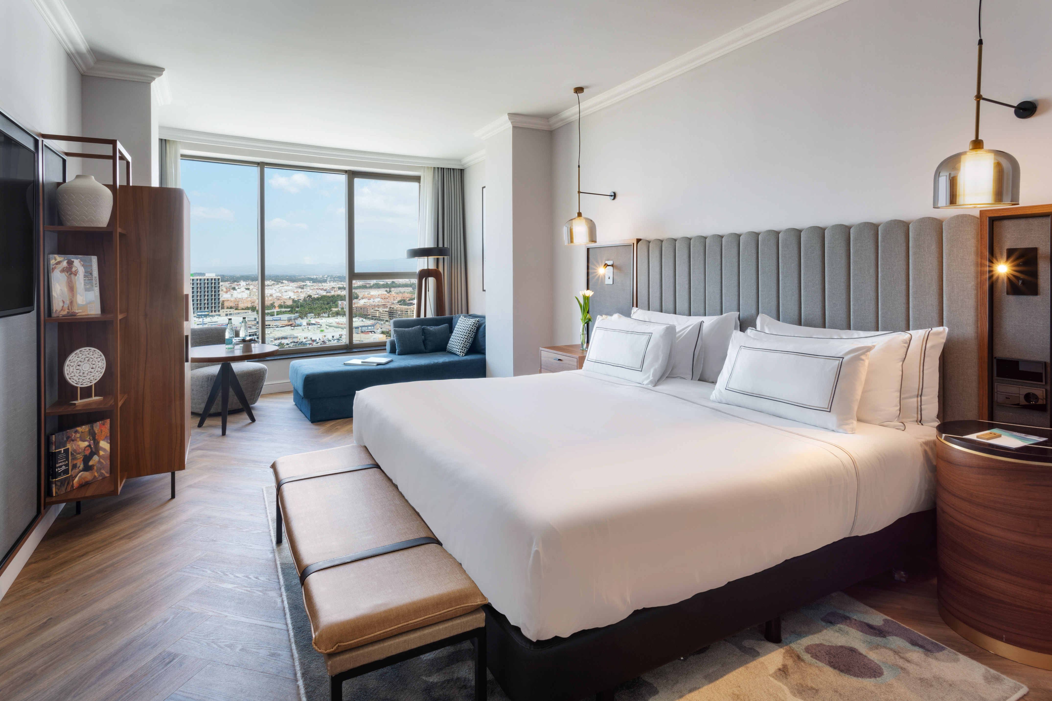 Suite de hotel moderna con cama grande, sofá y vistas panorámicas a la ciudad.