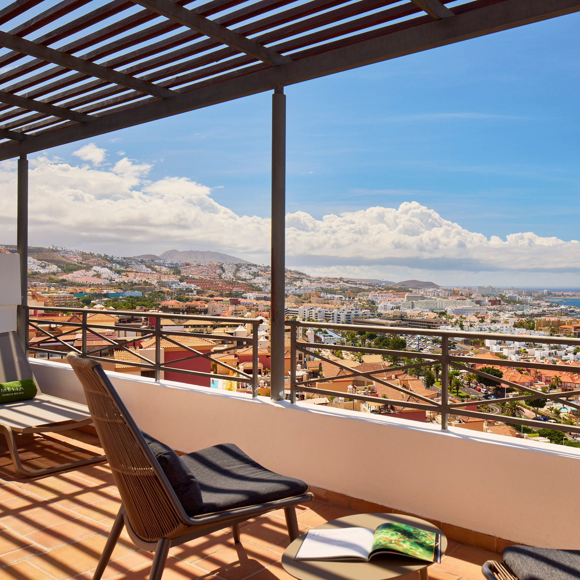 Balcony with lounge chairs, pergola, and coastal city ocean view.