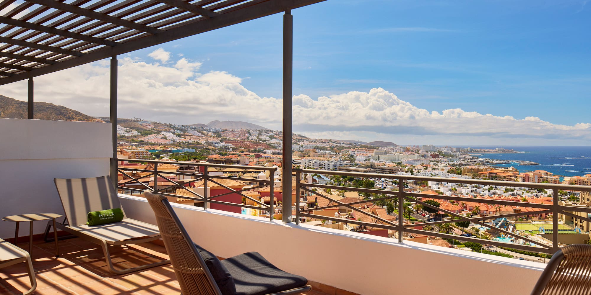 Balcony with lounge chairs, pergola, and coastal city ocean view.