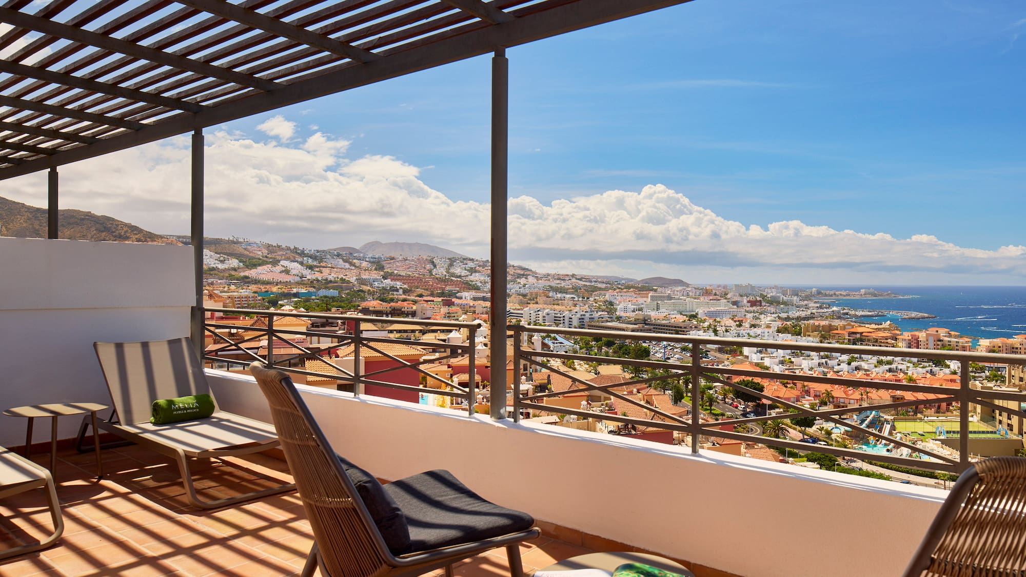 Balcony with lounge chairs, pergola, and coastal city ocean view.