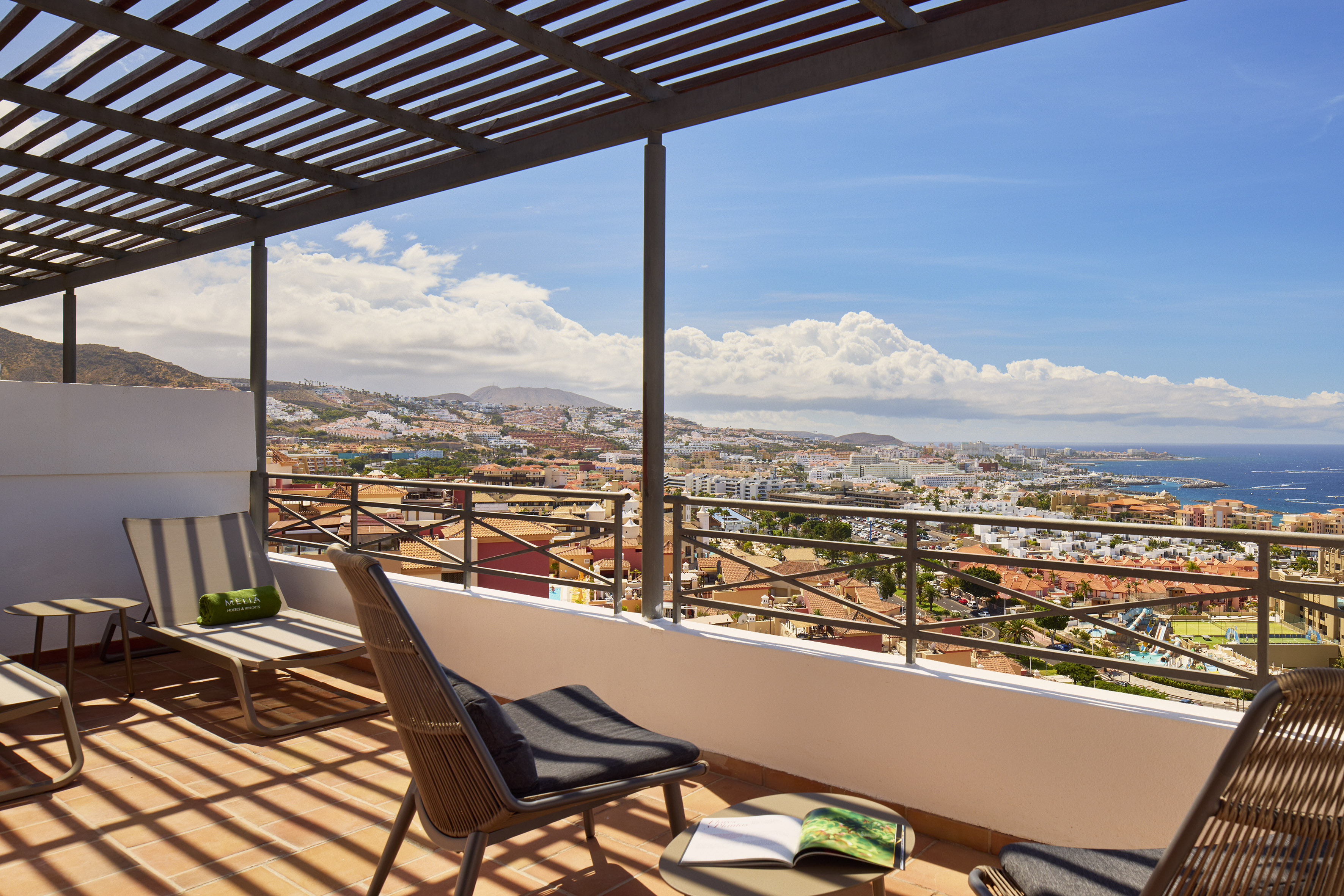 Balcony with lounge chairs, pergola, and coastal city ocean view.