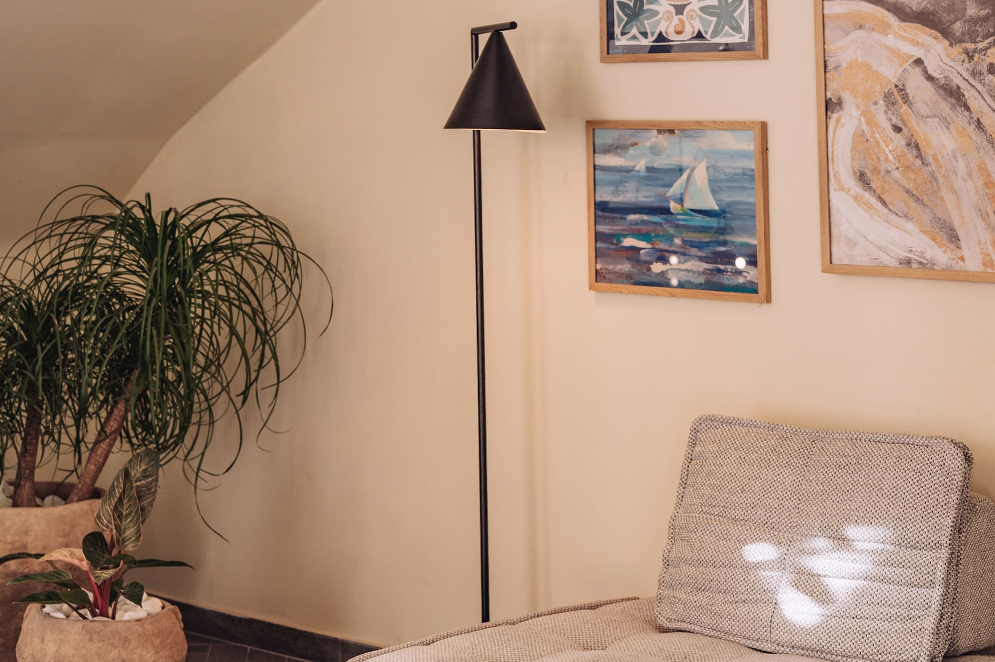 Modern lounge with textured sofa, floor lamp, potted plants, and framed coastal art.