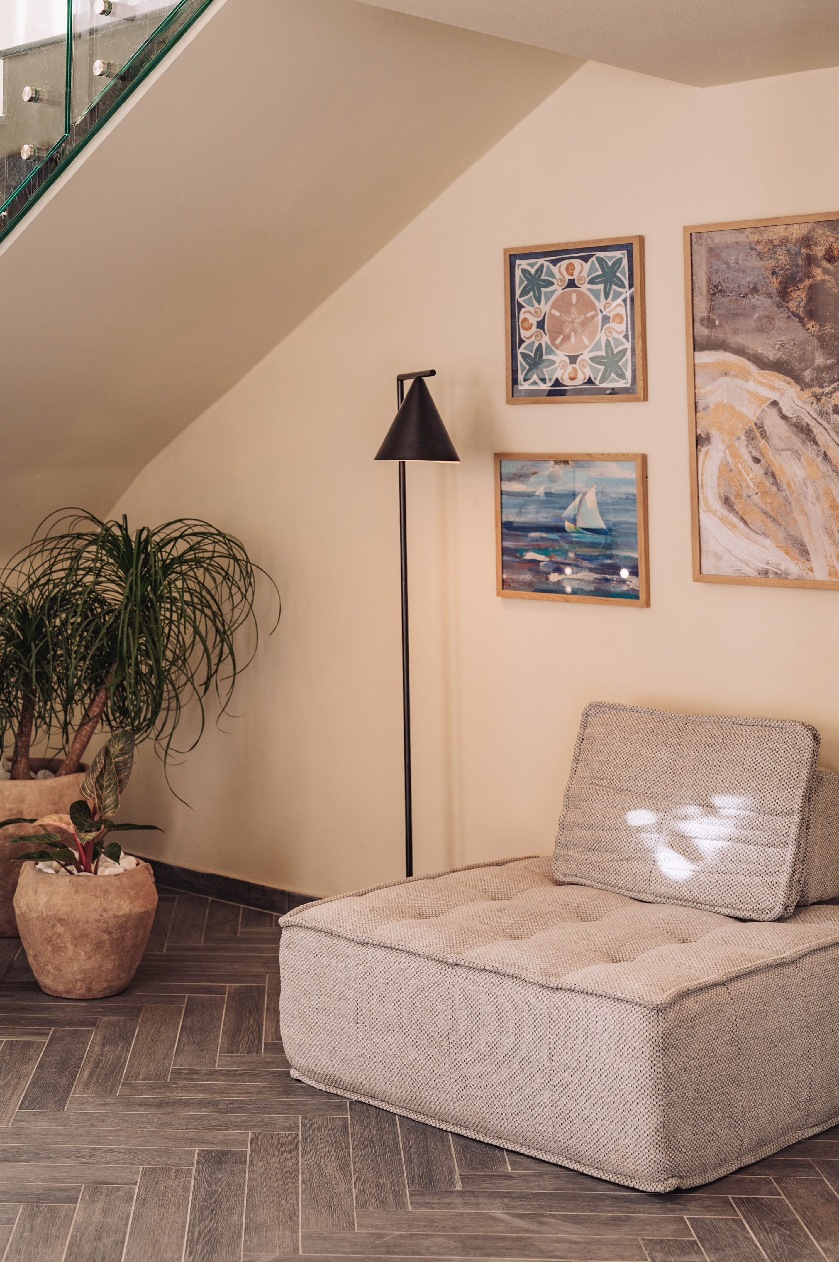 Modern lounge with textured sofa, floor lamp, potted plants, and framed coastal art.