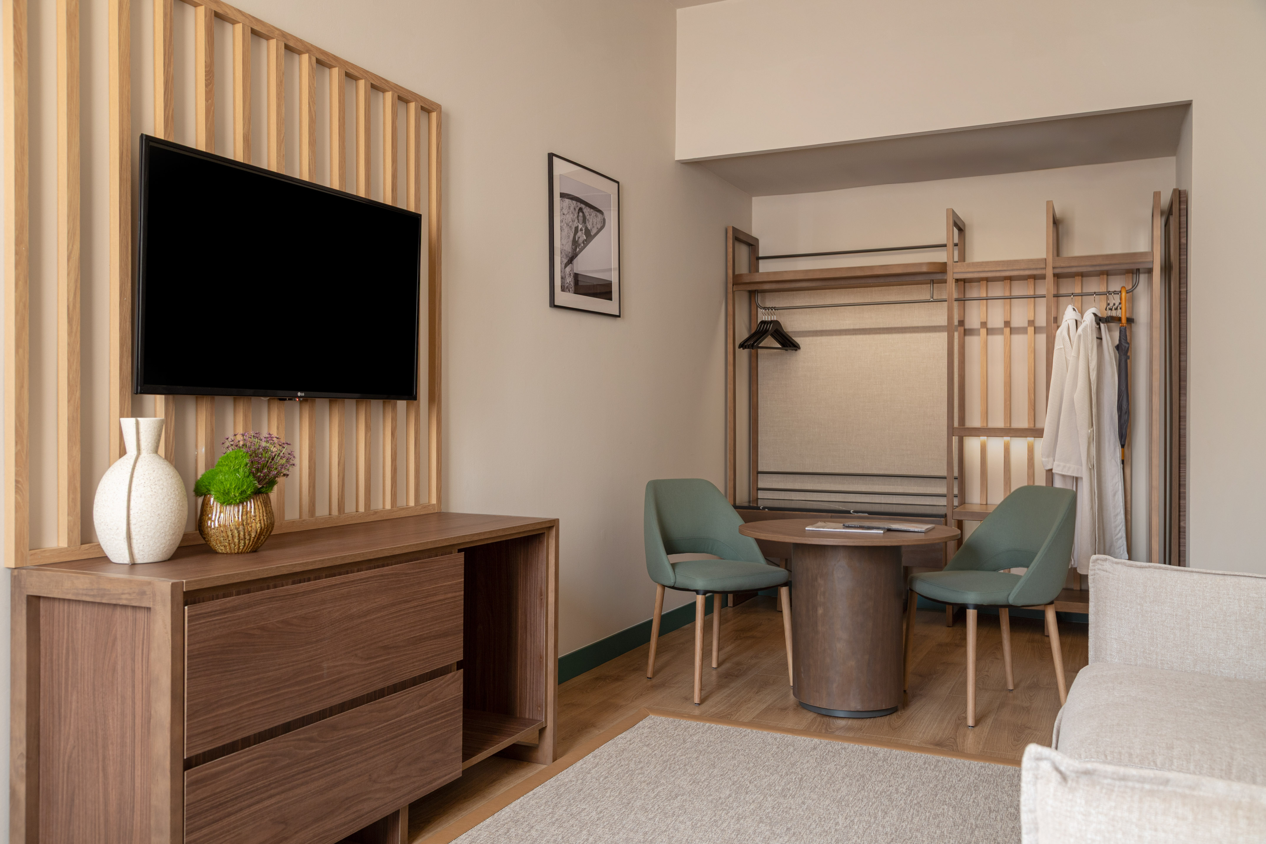 Modern hotel guest room with TV, workspace, and open closet storage.