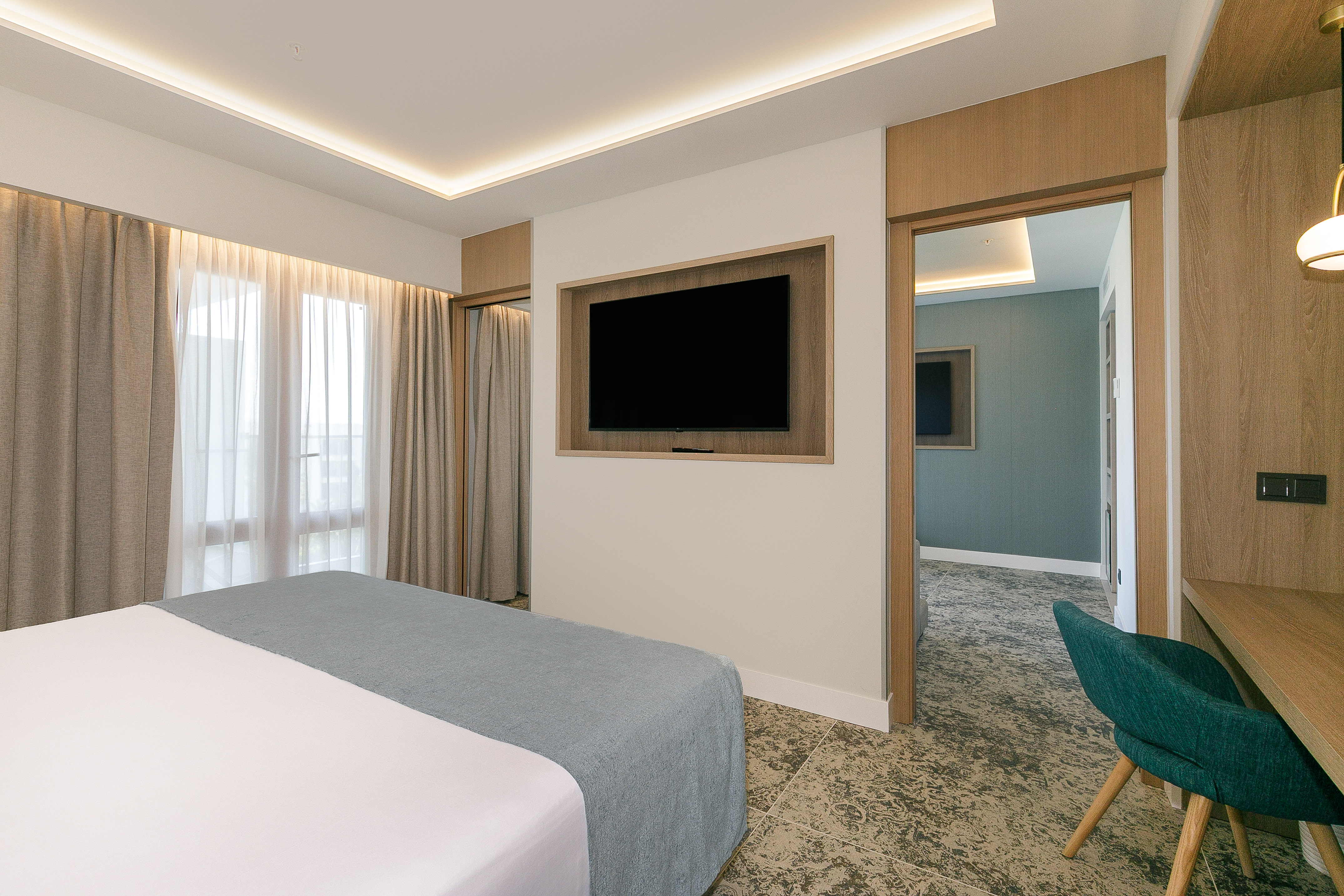 Modern hotel bedroom with comfortable bed, built-in TV, and work desk.