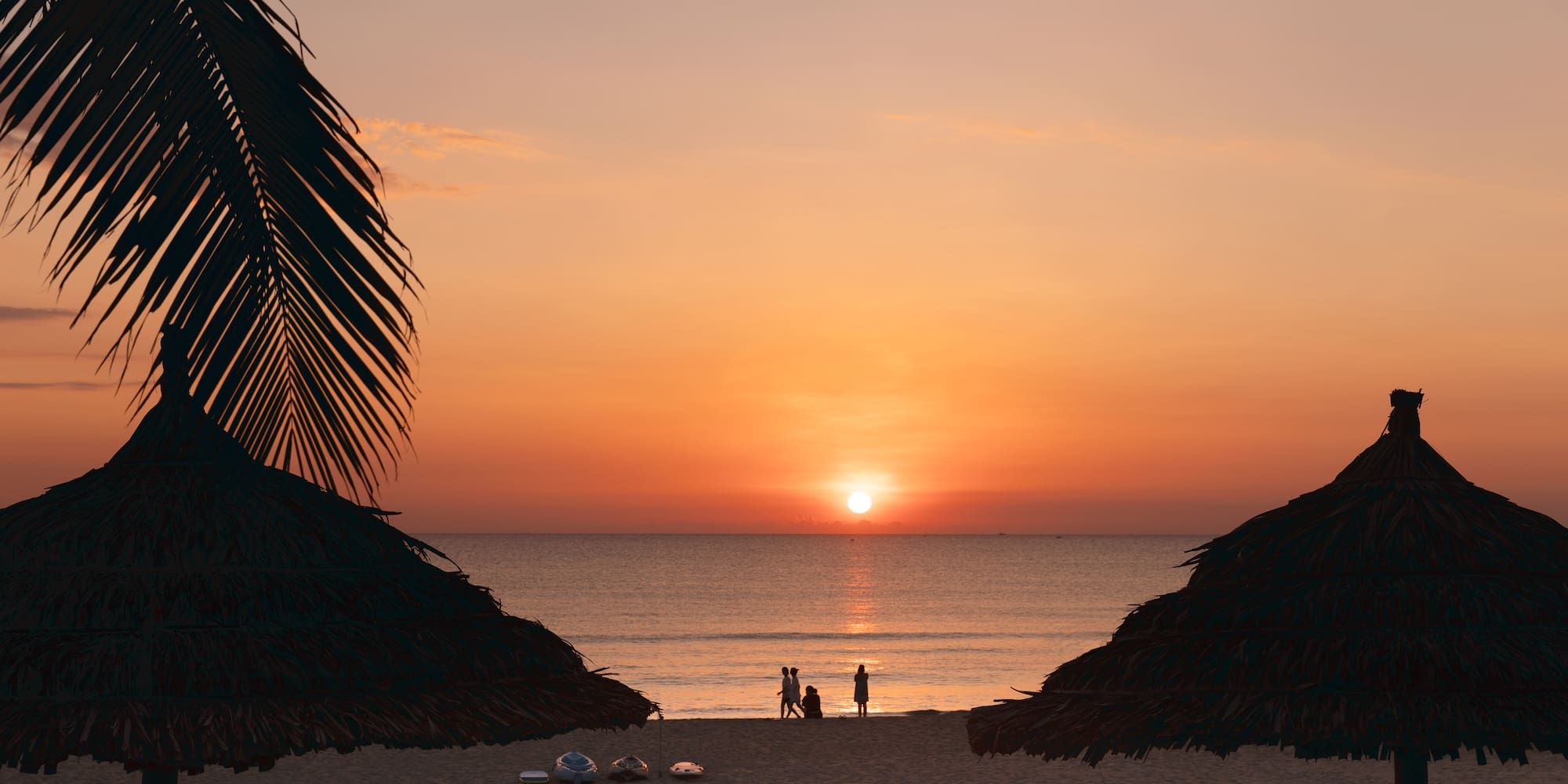 a group of people on a beach with umbrellas and a sunset