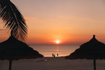 a group of people on a beach with umbrellas and a sunset