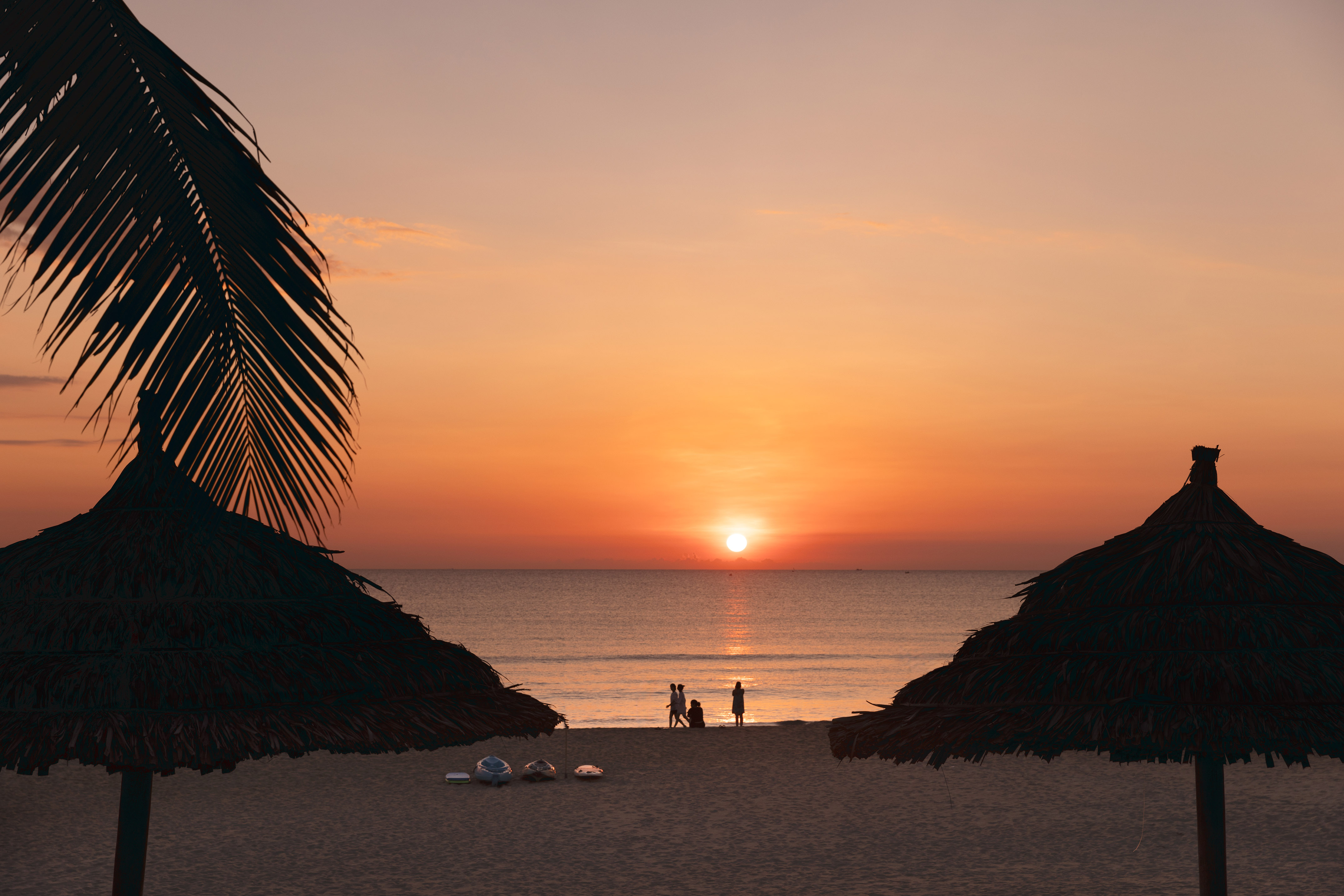 a group of people on a beach with umbrellas and a sunset