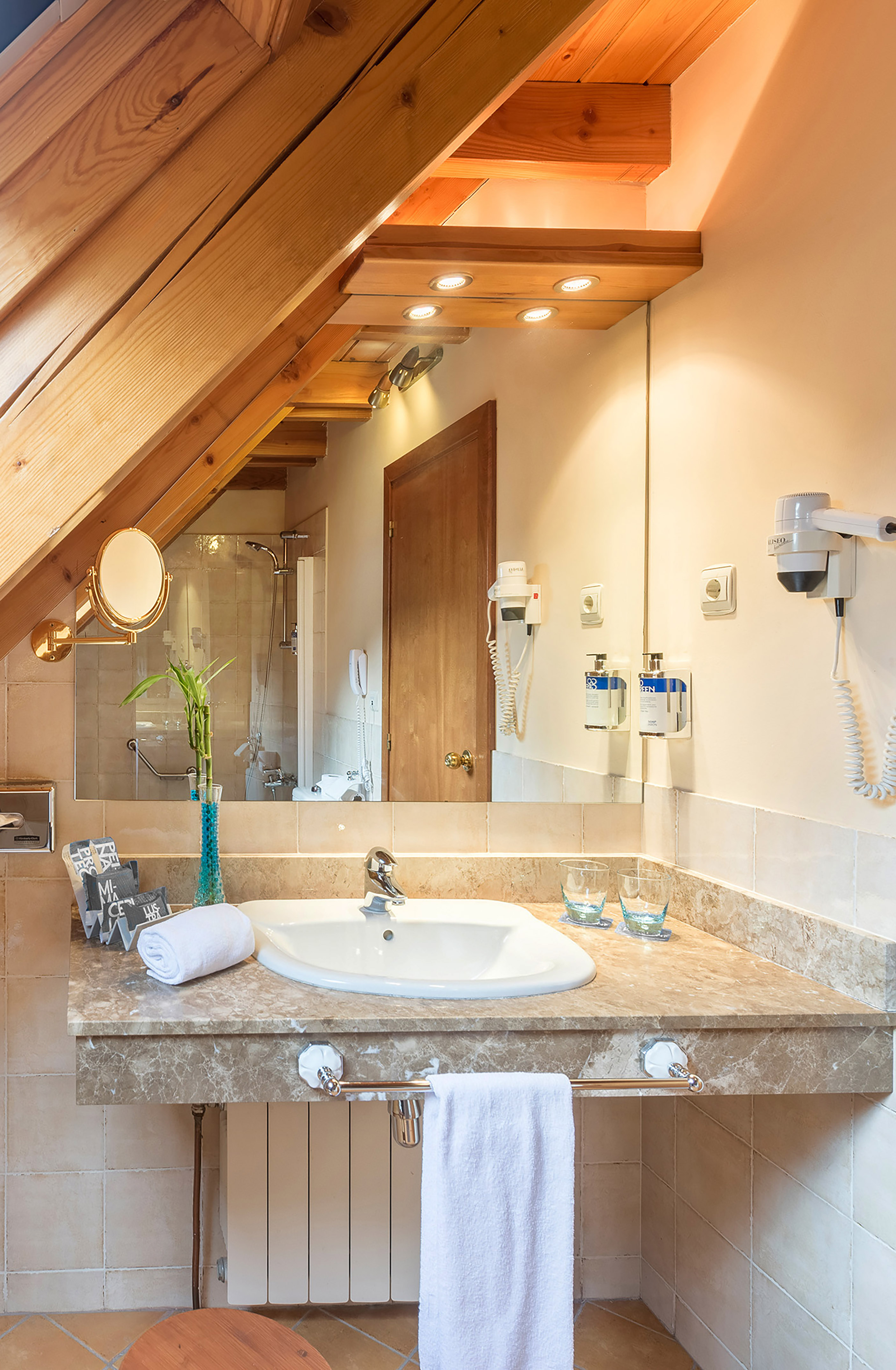 Sloped ceiling bathroom vanity with wooden beams, marble countertop, and sink.