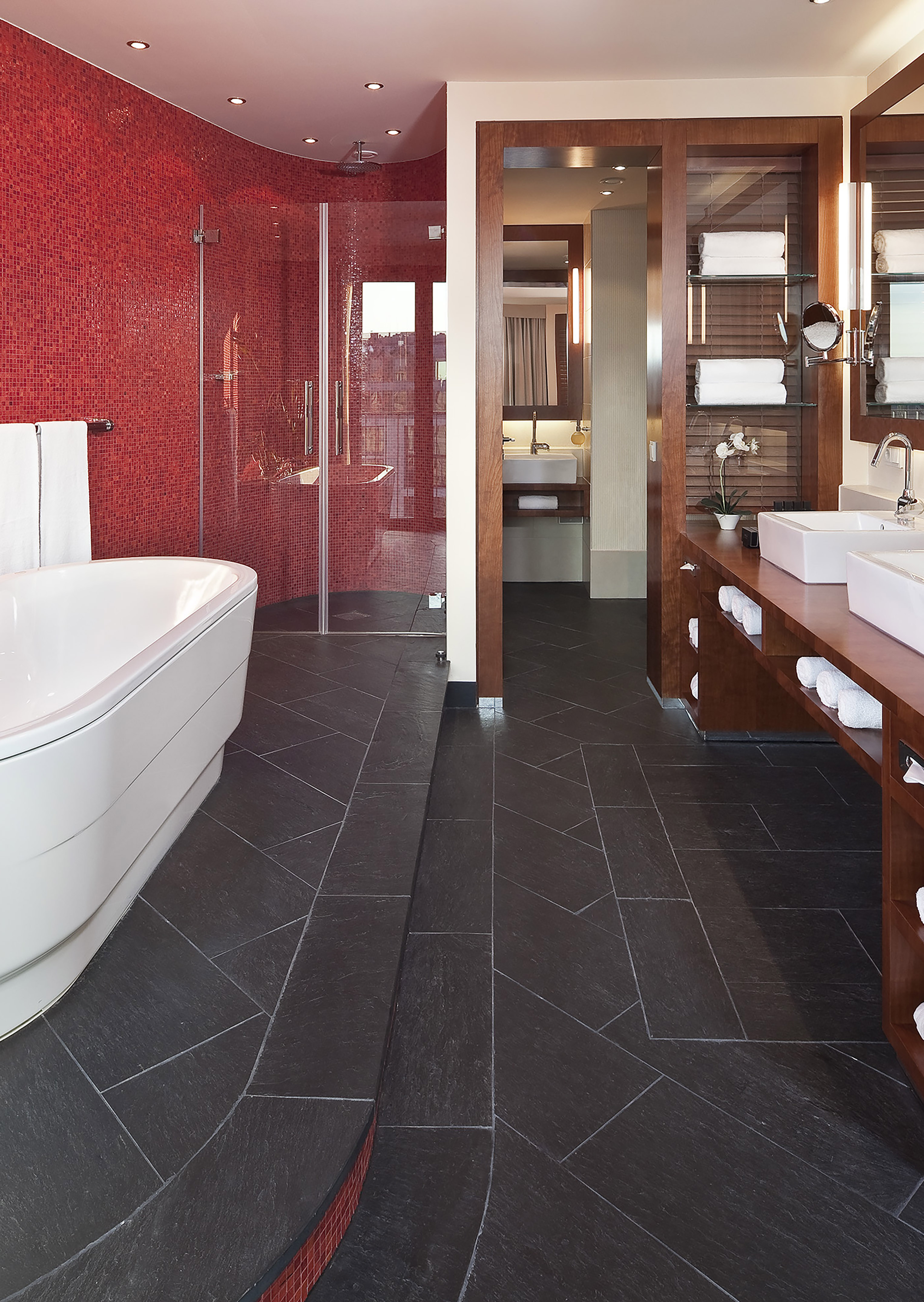 Red mosaic luxury bathroom with freestanding tub, dark floor, and wood double vanity.