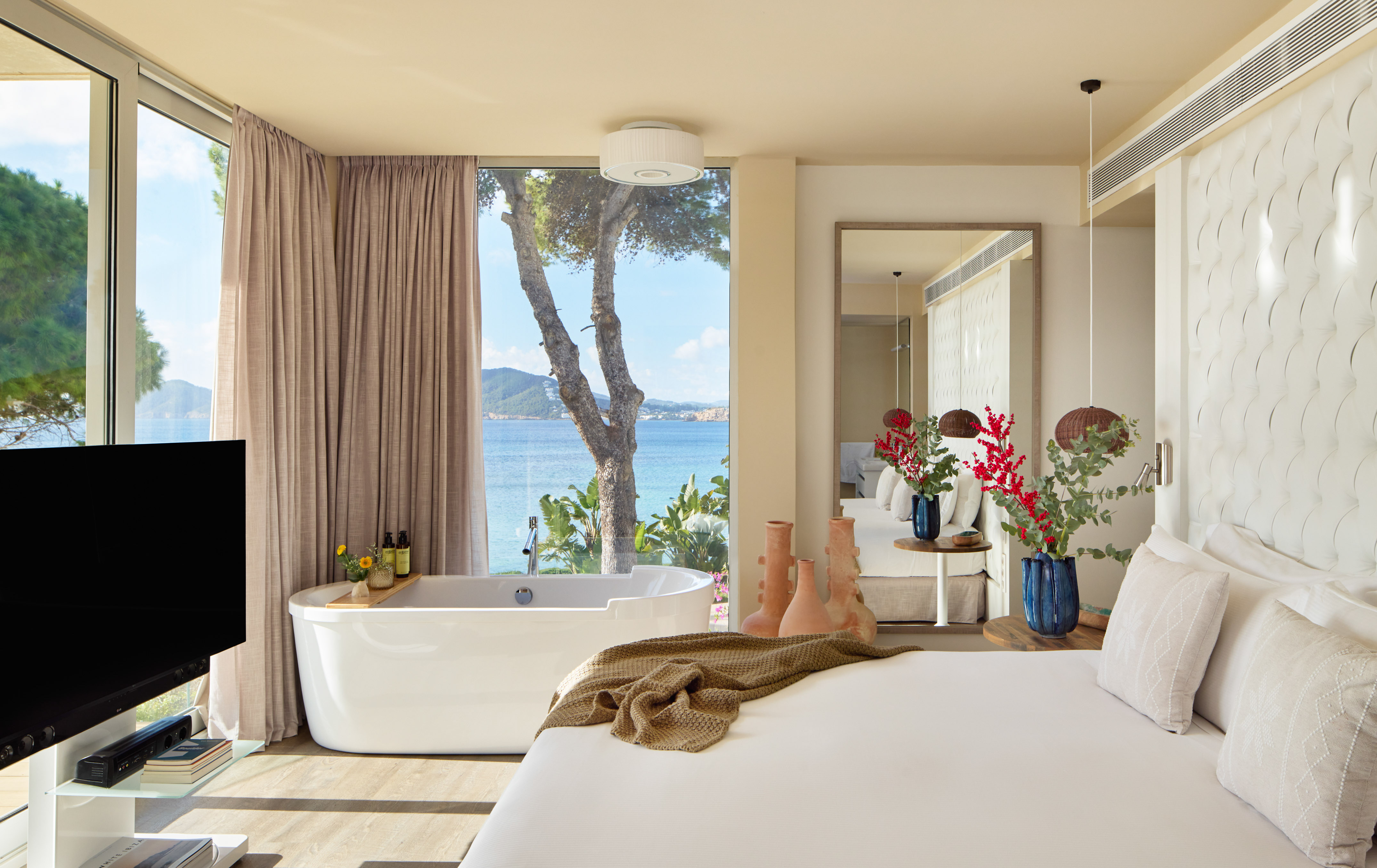 Luxury hotel bedroom with sea view, freestanding bathtub, and modern white bed.
