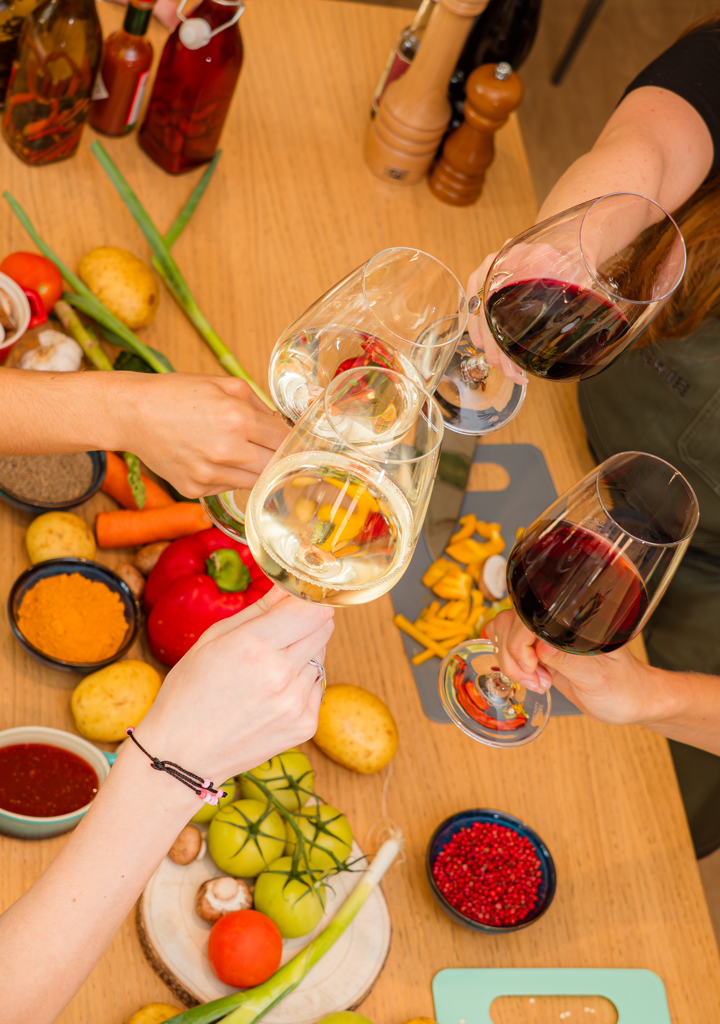 Four hands clinking wine glasses over fresh kitchen ingredients and spices.