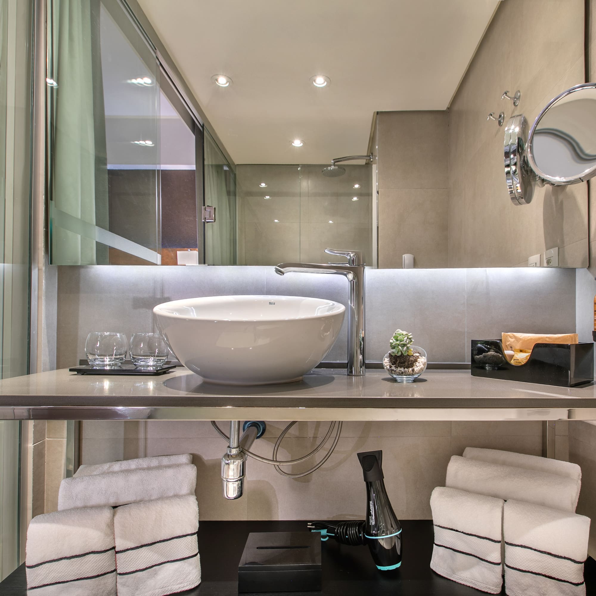 Banheiro moderno com pia de cuba branca sobre bancada de inox, espelho e toalhas organizadas. - Grand Premium - Meliá Ibirapuera, São Paulo