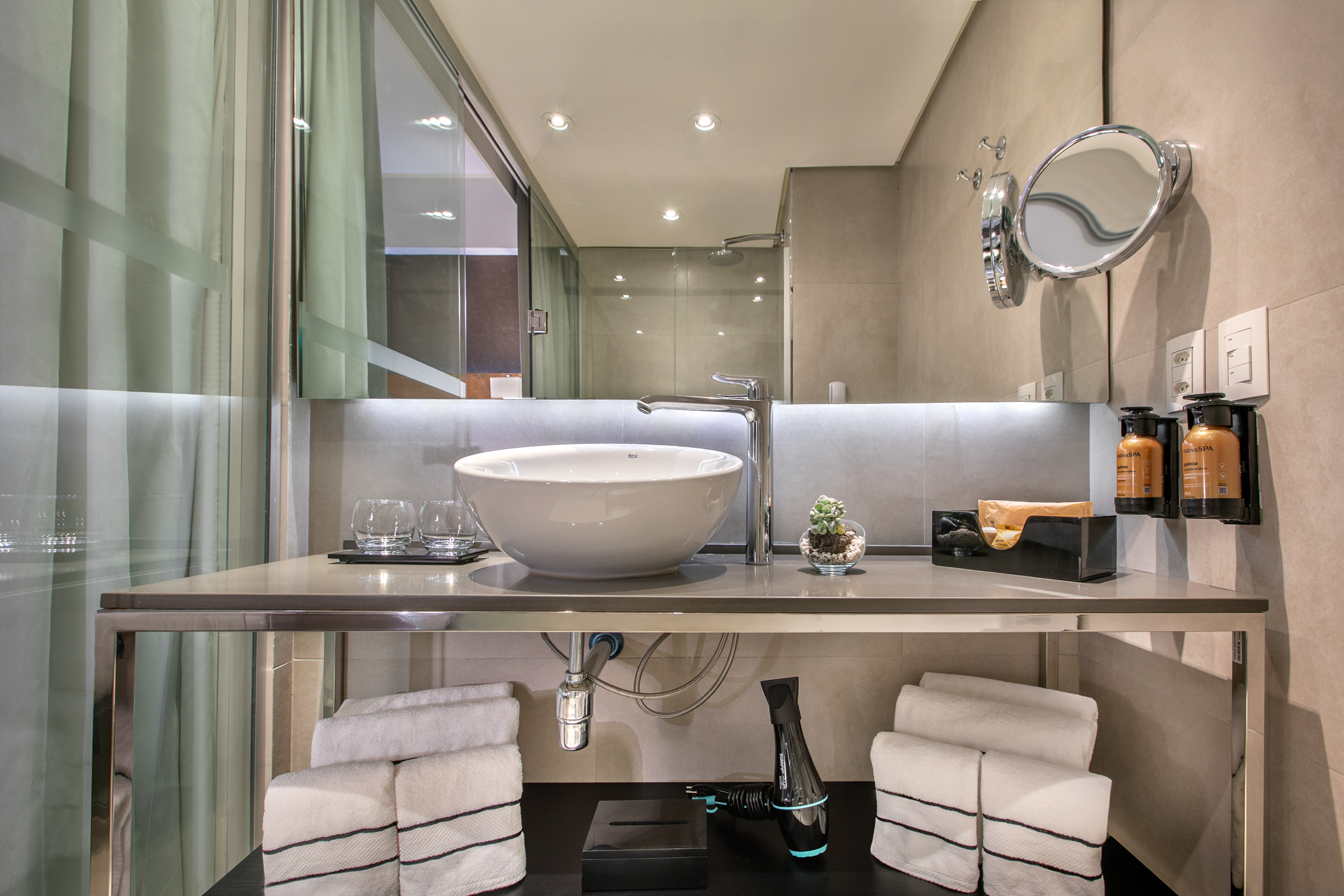 Banheiro moderno com pia de cuba branca sobre bancada de inox, espelho e toalhas organizadas. - Grand Premium - Meliá Ibirapuera, São Paulo