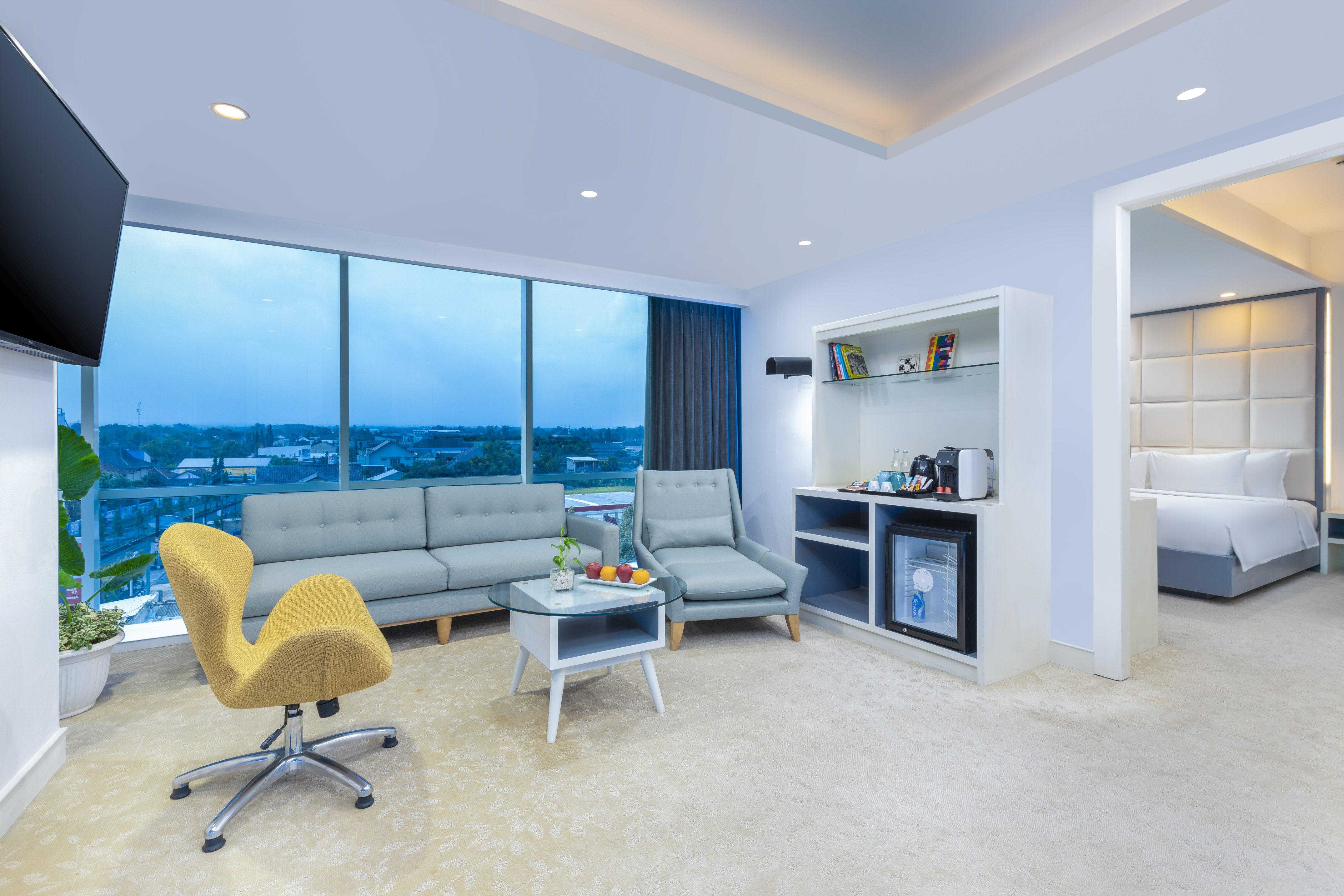 Modern hotel suite with living area, city view, mini-bar, and bedroom.