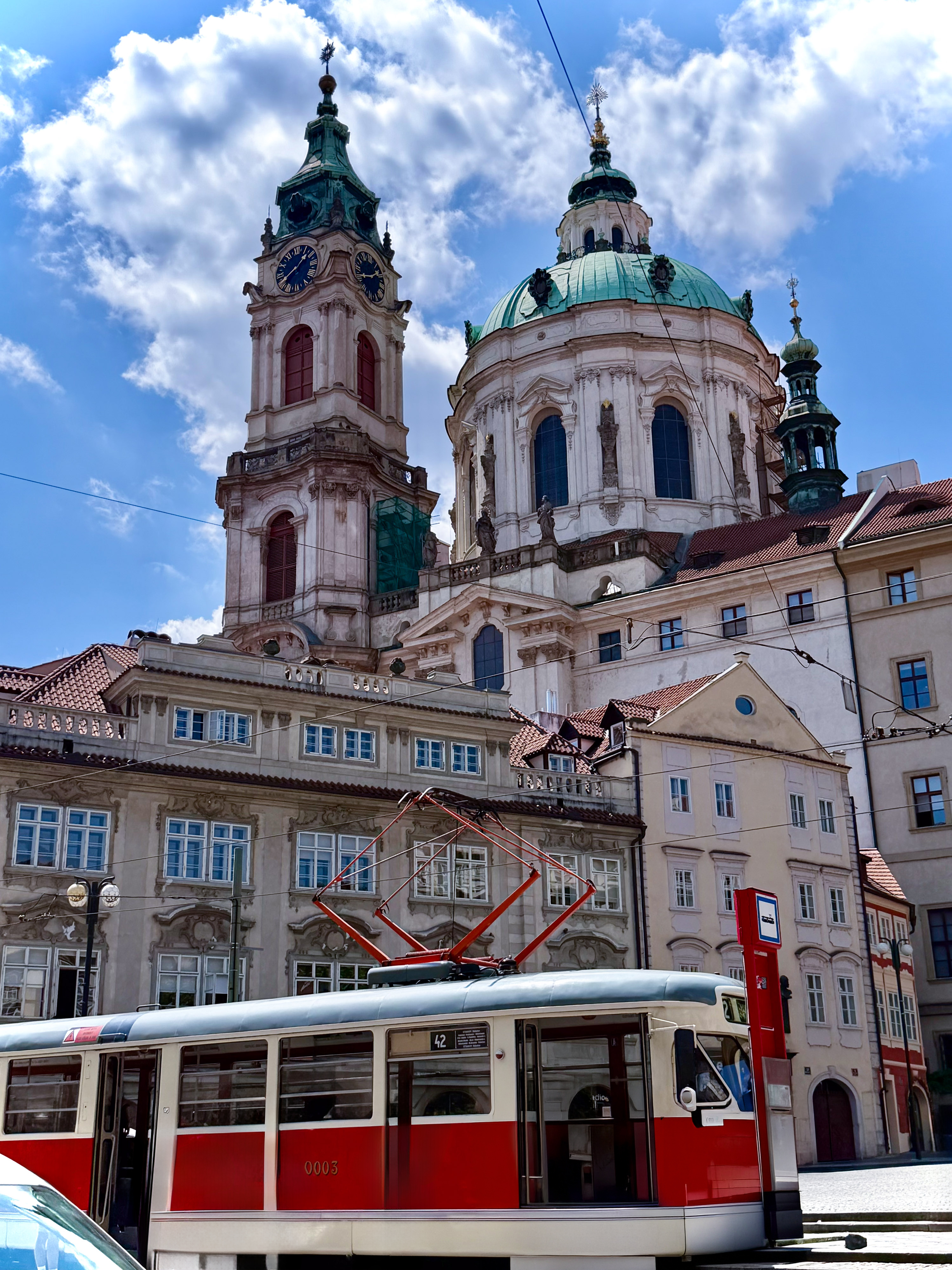 Red and white Prague tram in front of historic St. Nicholas Church.