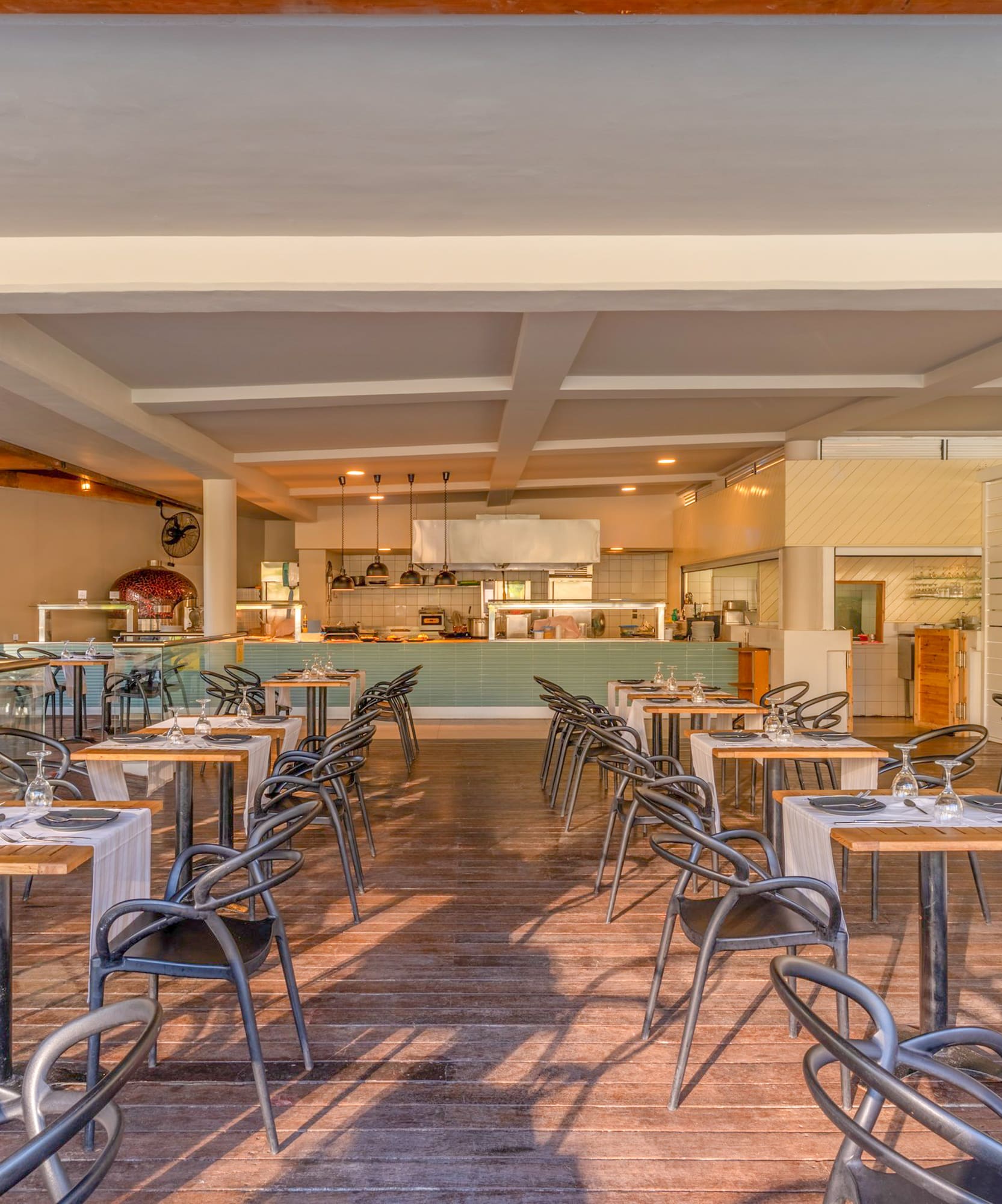 Outdoor restaurant dining area with open kitchen, pizza oven, and set tables.