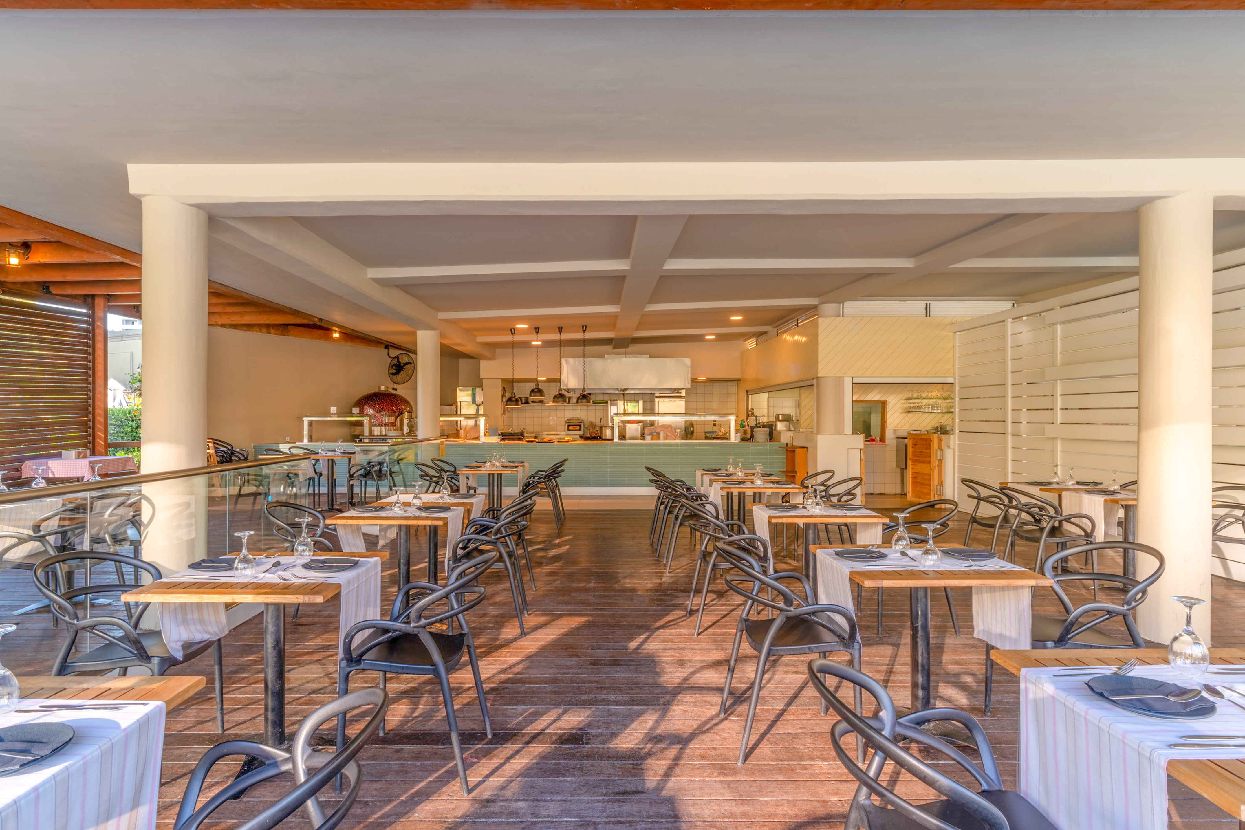 Outdoor restaurant dining area with open kitchen, pizza oven, and set tables.