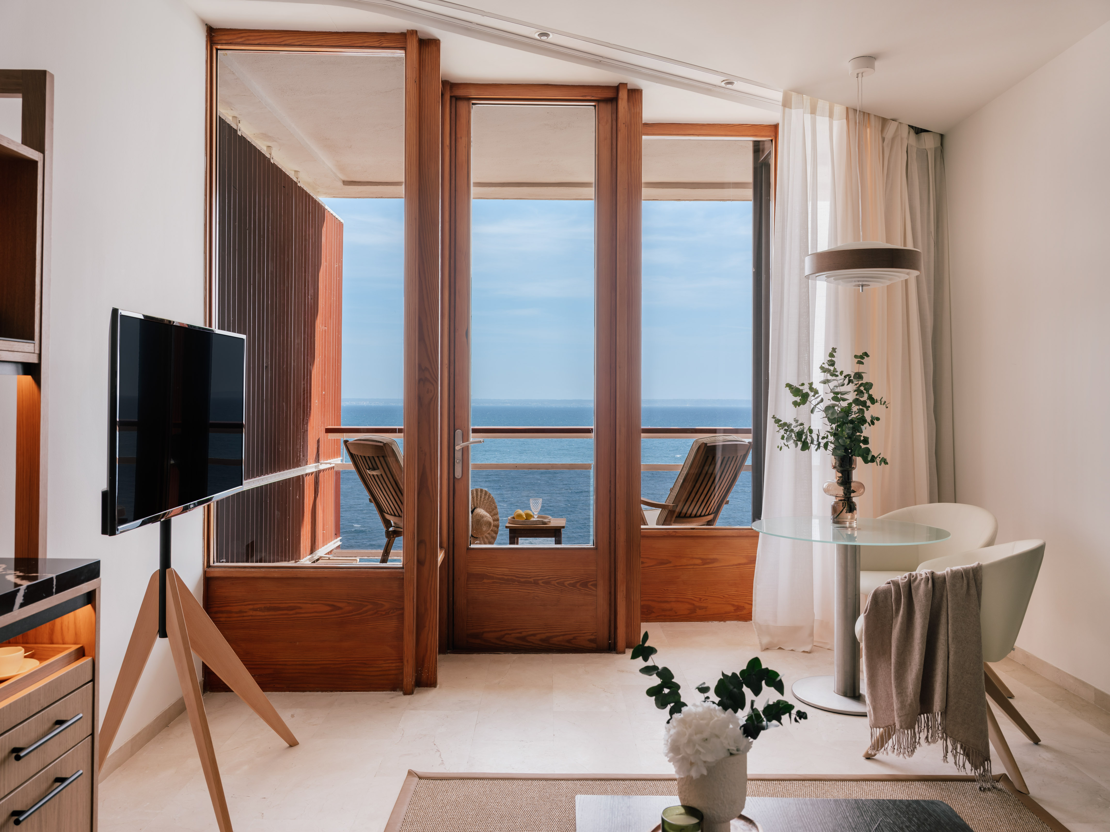 Modern hotel room with ocean view balcony, wood doors, and living area.