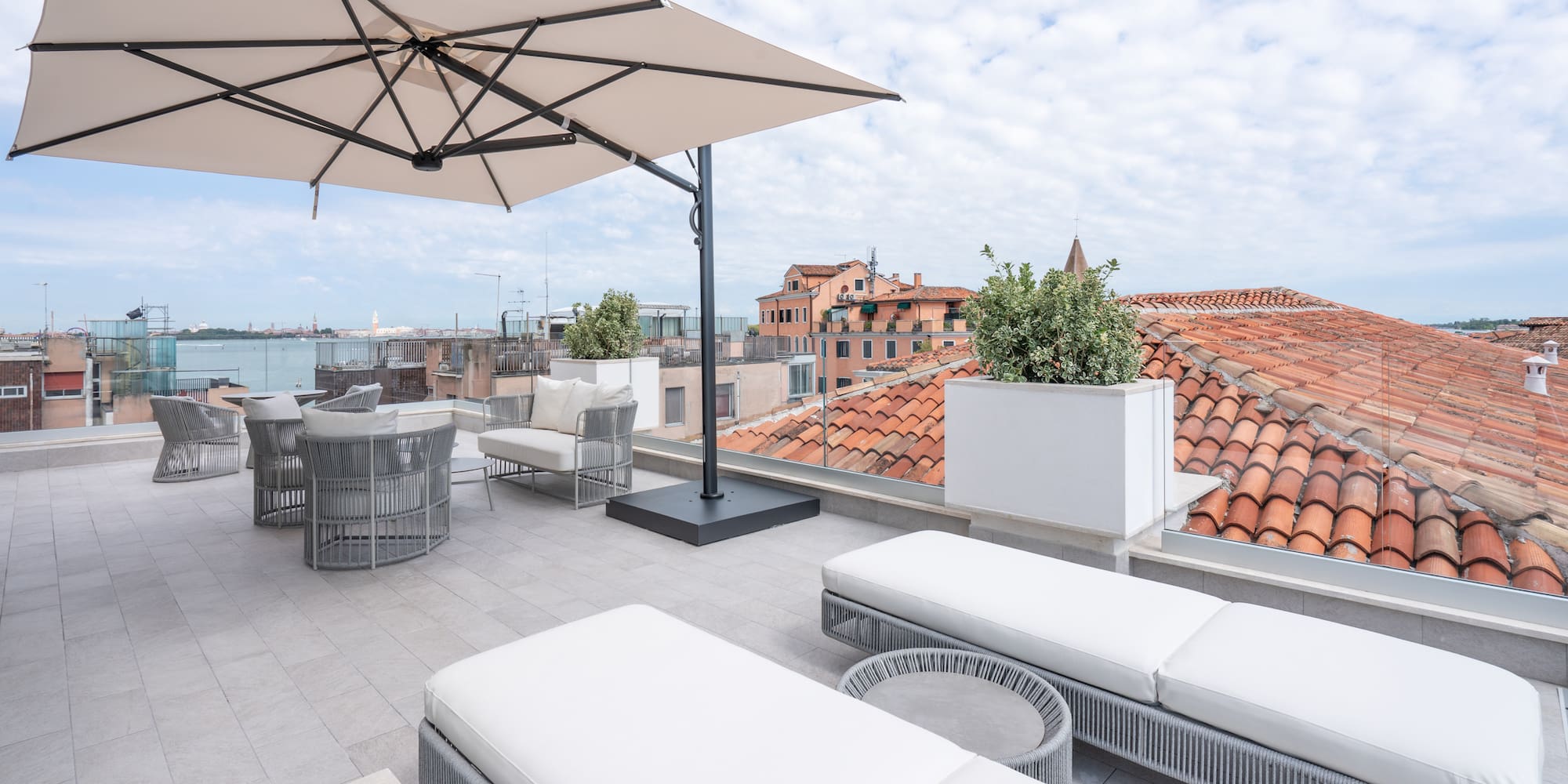 Rooftop terrace in Venice with sun loungers, umbrella, and cityscape.
