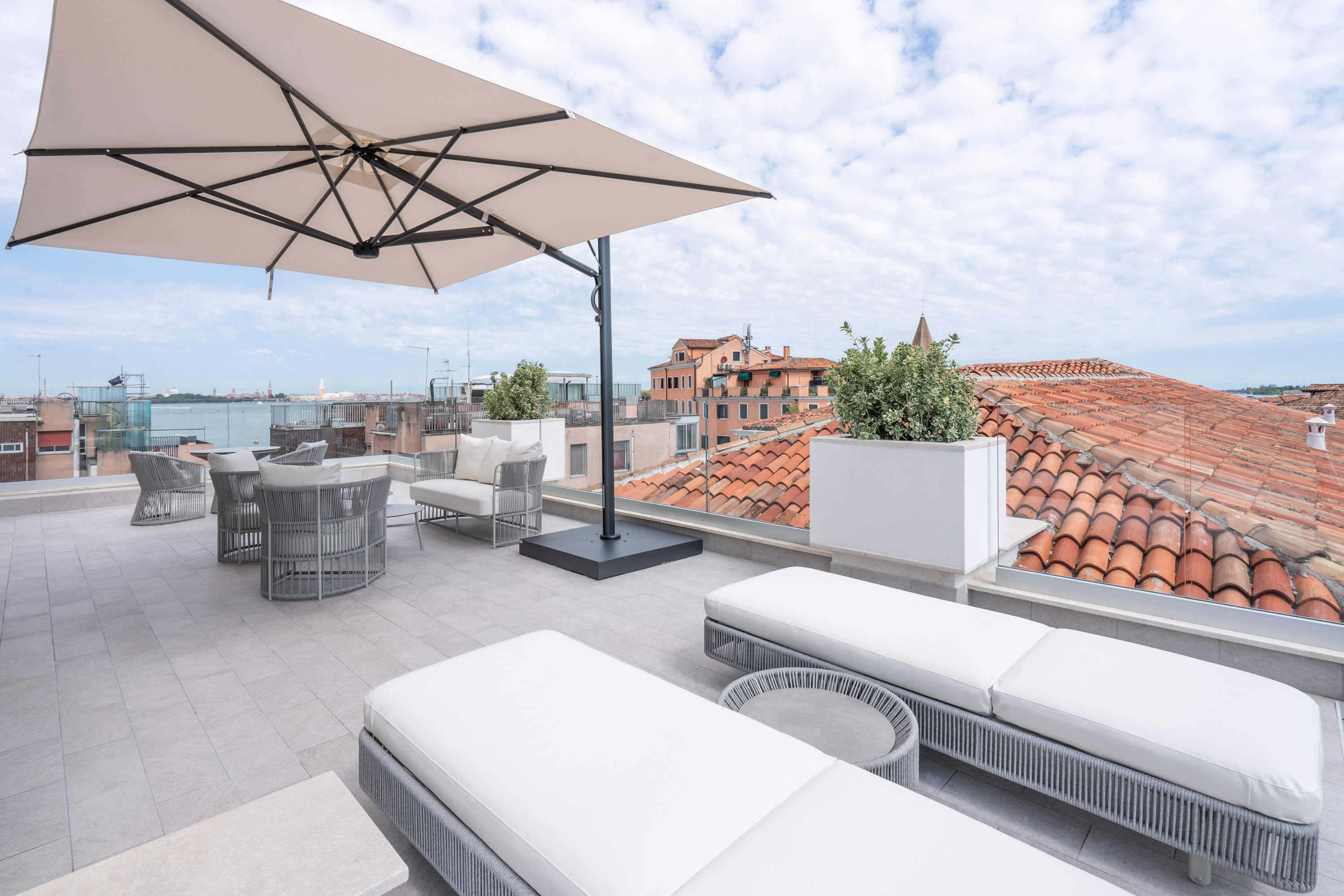 Rooftop terrace in Venice with sun loungers, umbrella, and cityscape.
