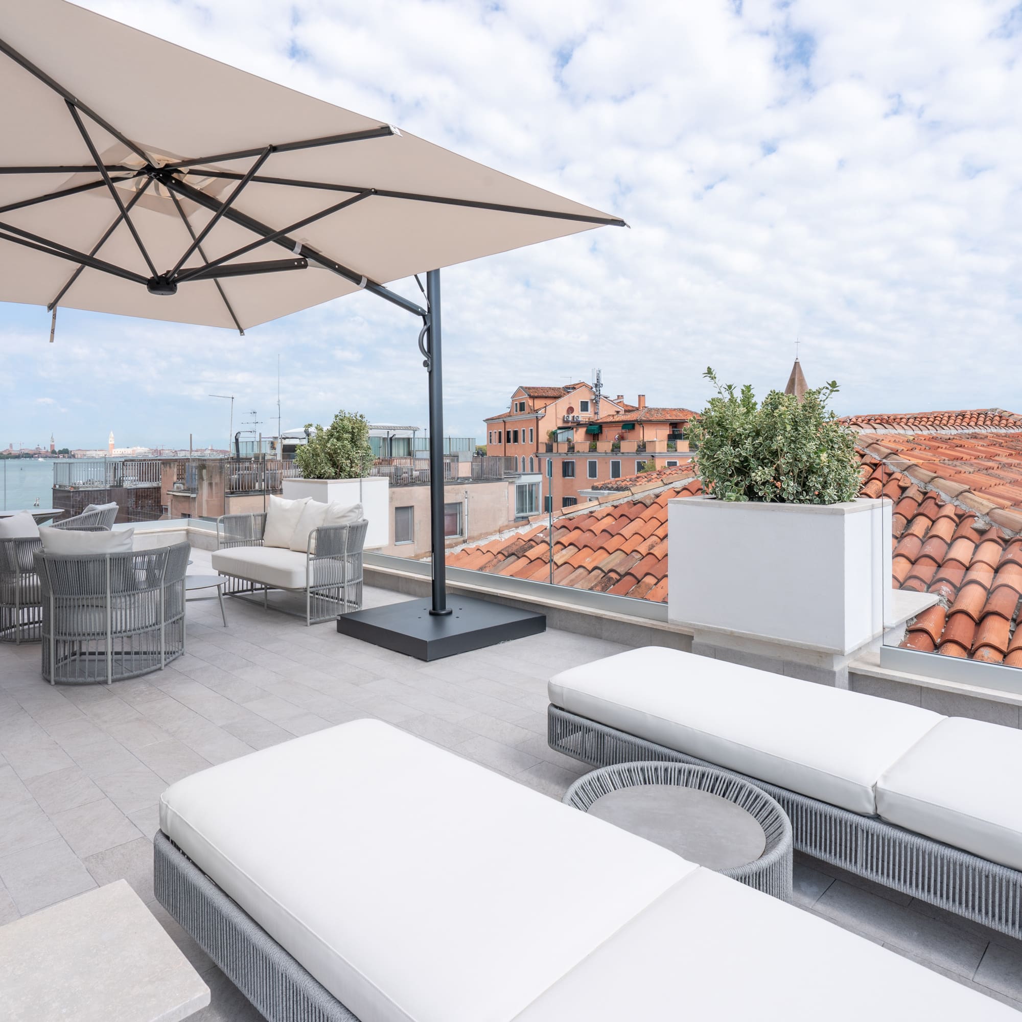 Rooftop terrace in Venice with sun loungers, umbrella, and cityscape.