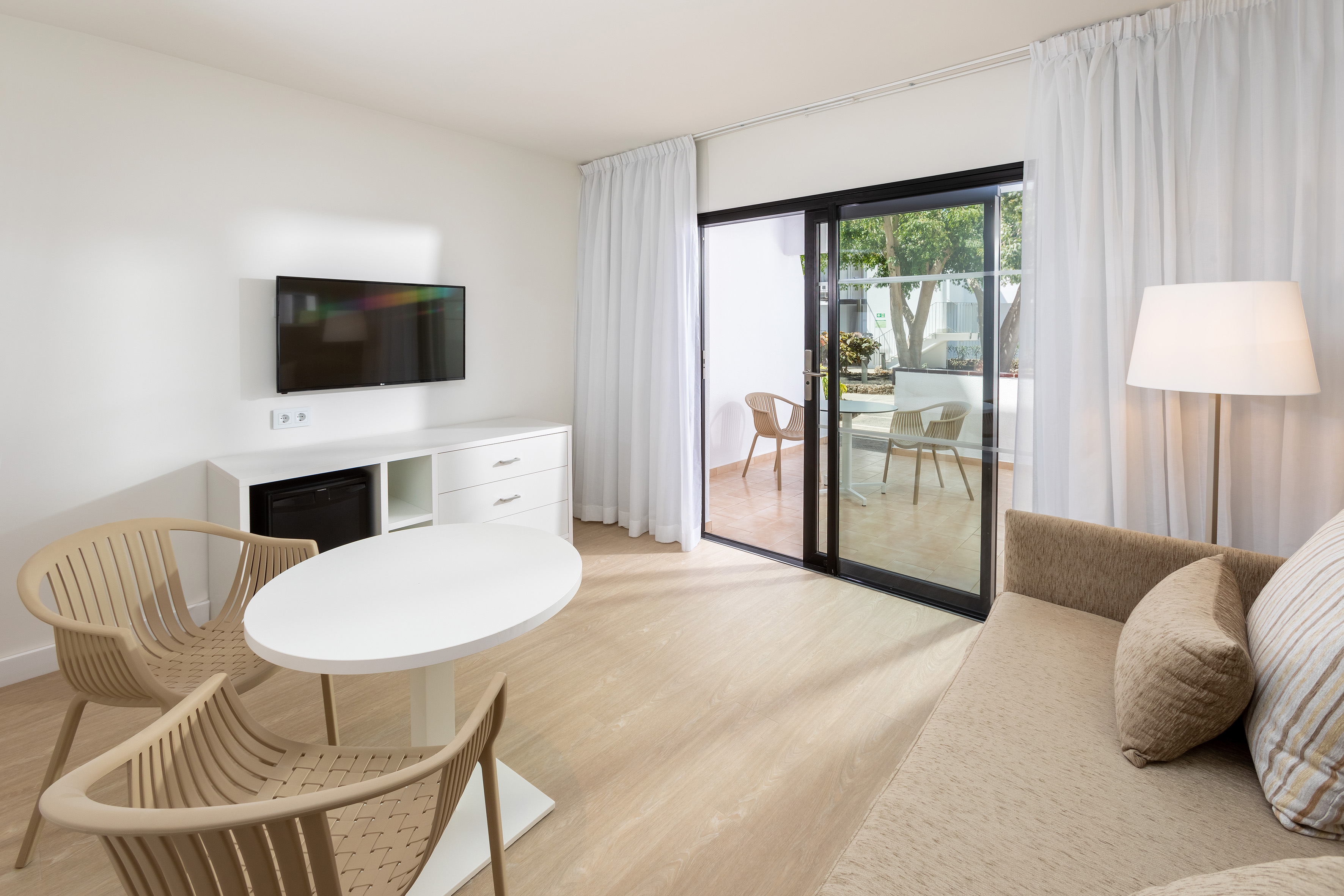Modern hotel room living area with TV, sofa, and balcony access.