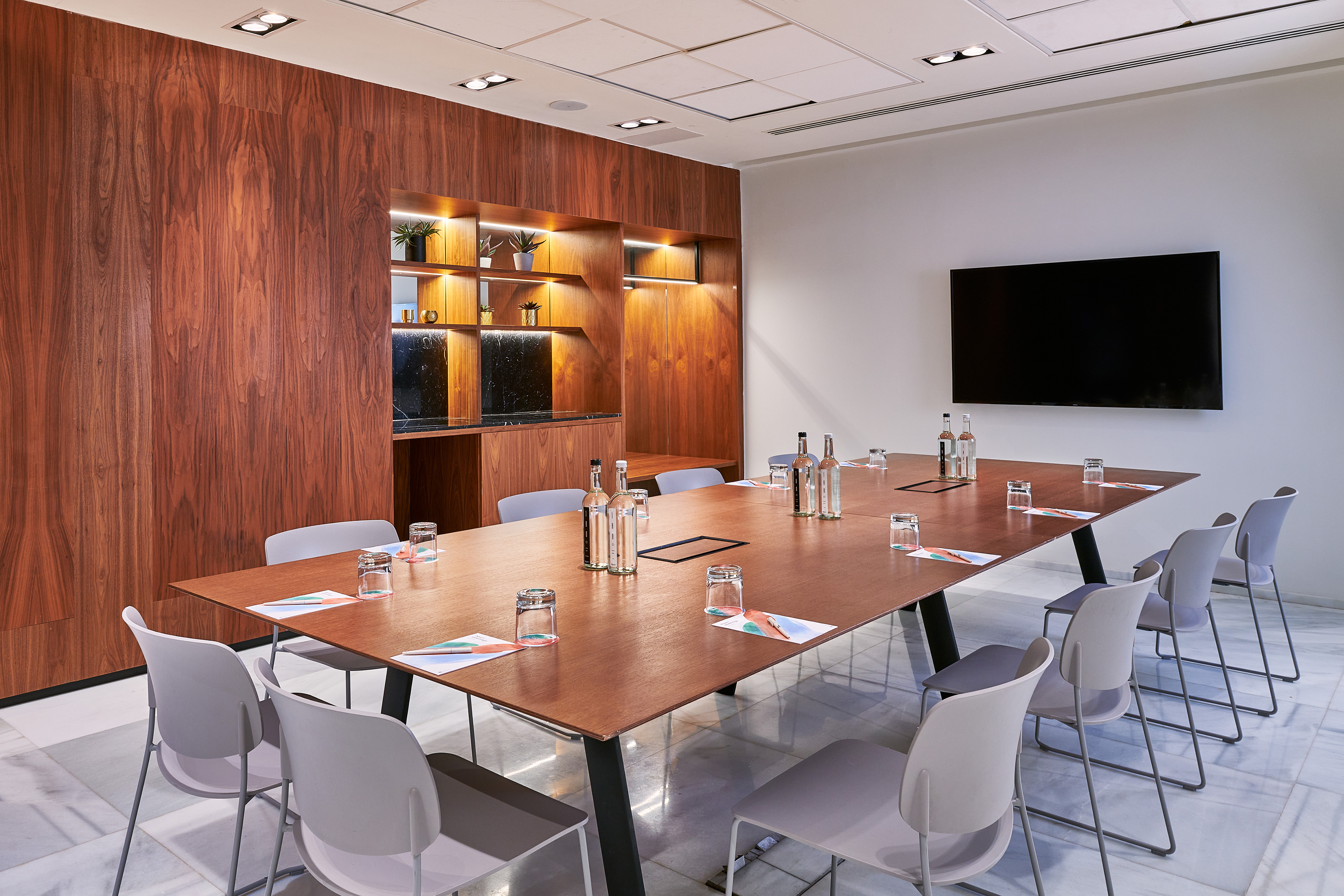 Modern meeting room with wood paneling, long table, grey chairs, and wall-mounted TV.