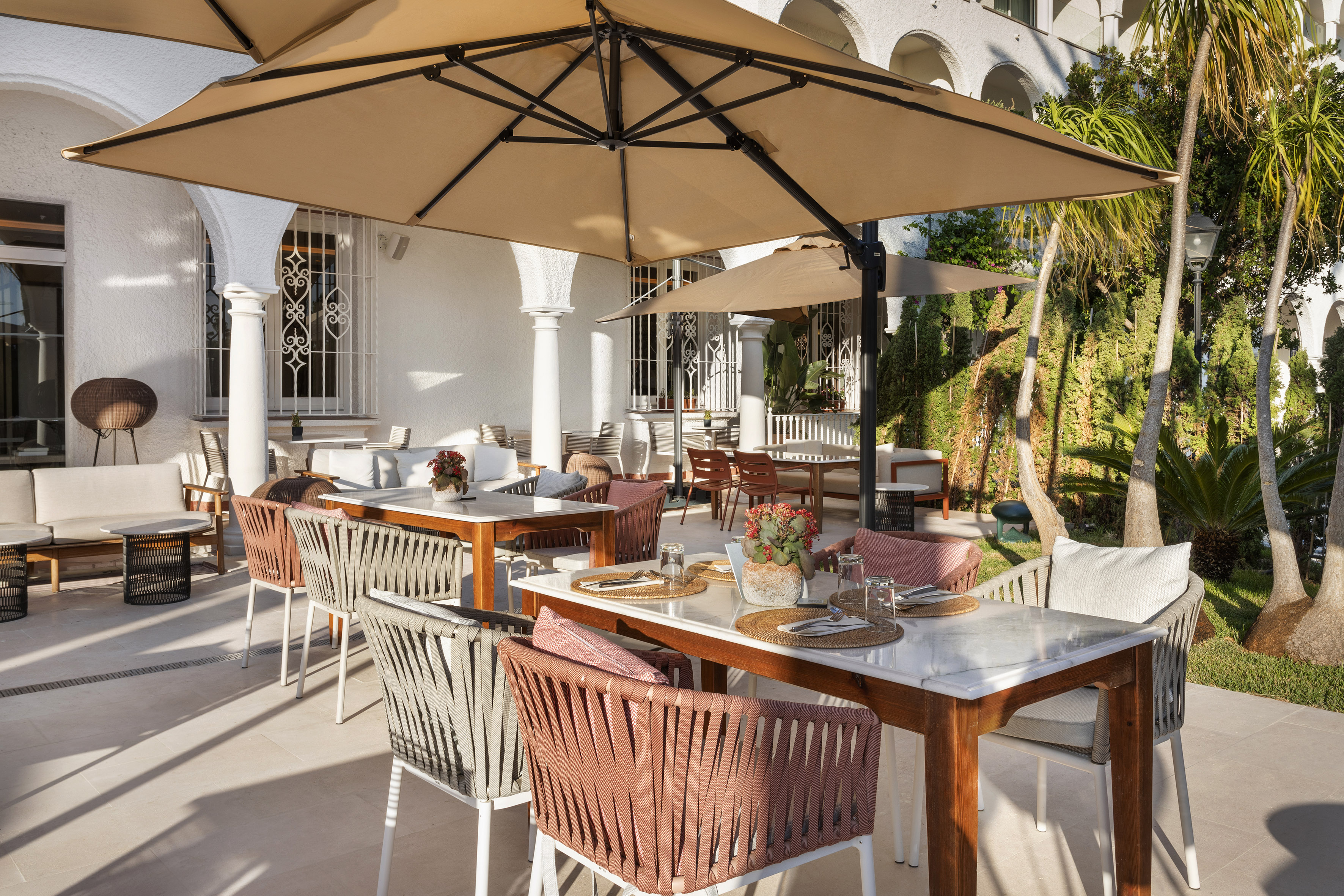 Luxury hotel patio with modern dining tables, sun umbrellas, and lush palms.